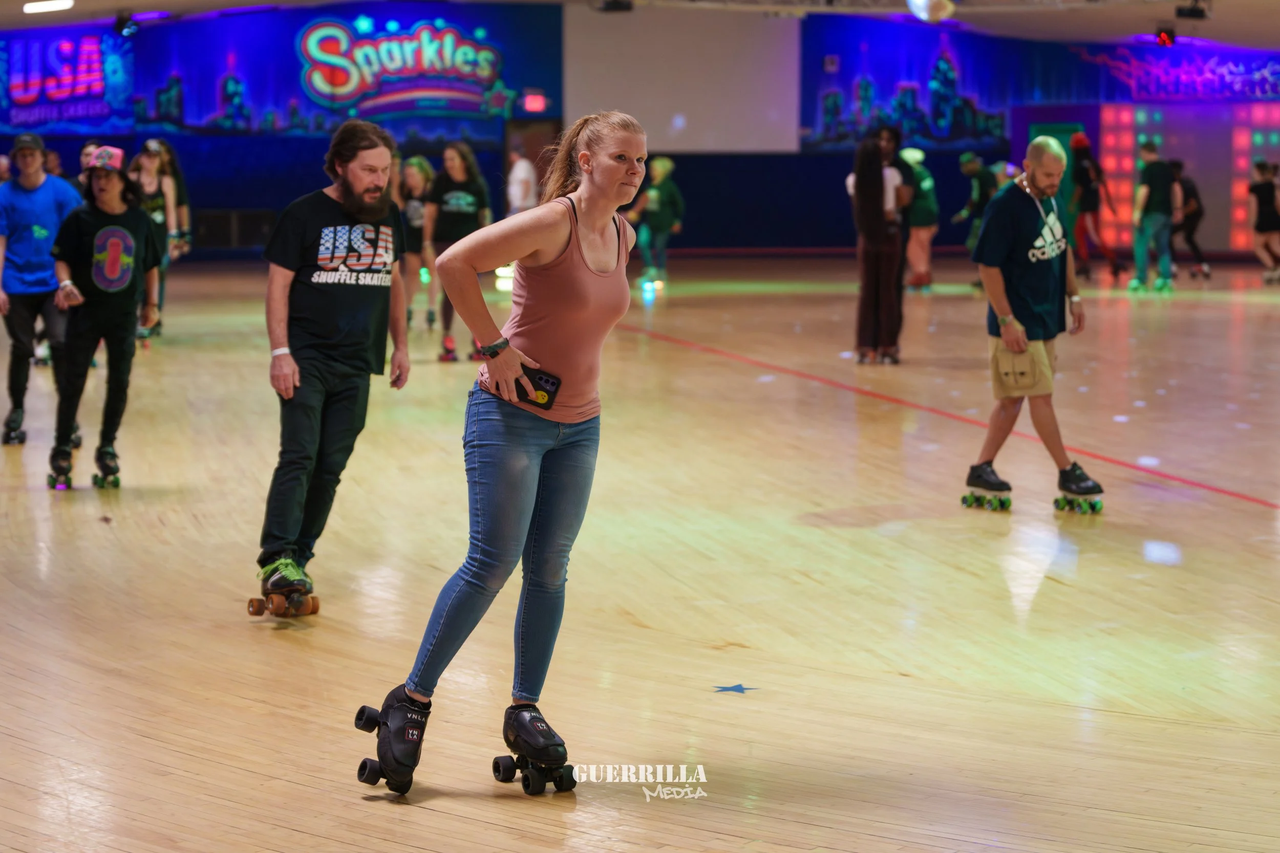 People roller skating at an indoor roller rink with colorful neon lights and a vibrant backdrop.