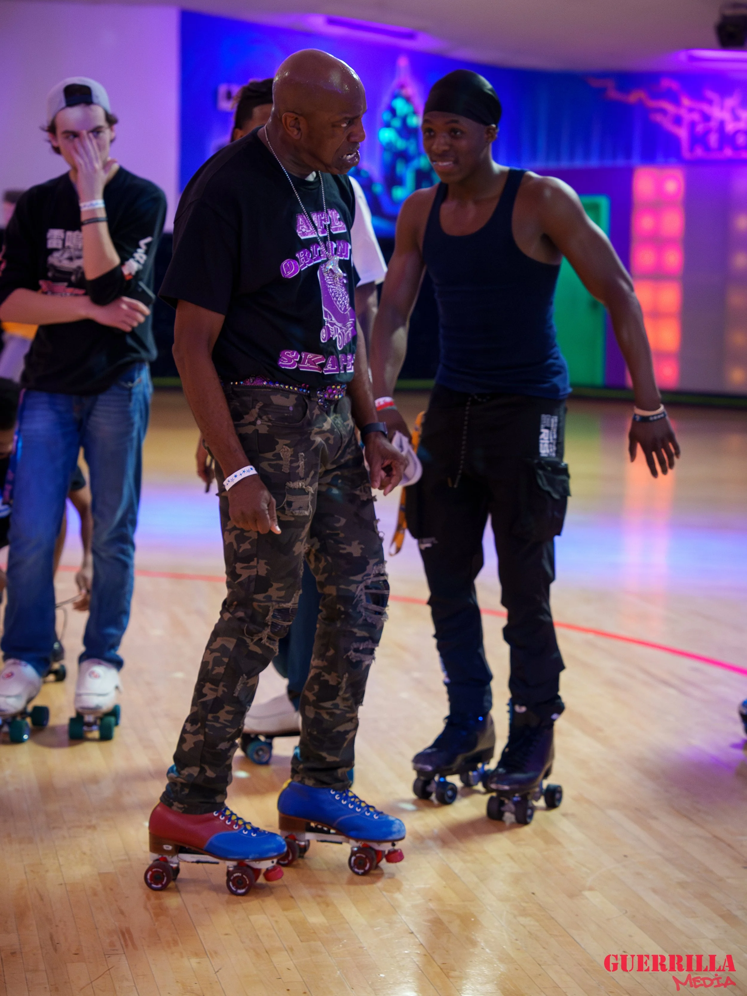 A group of people roller skating indoors with colorful neon lights in the background, including an older man and a young woman engaged in conversation.