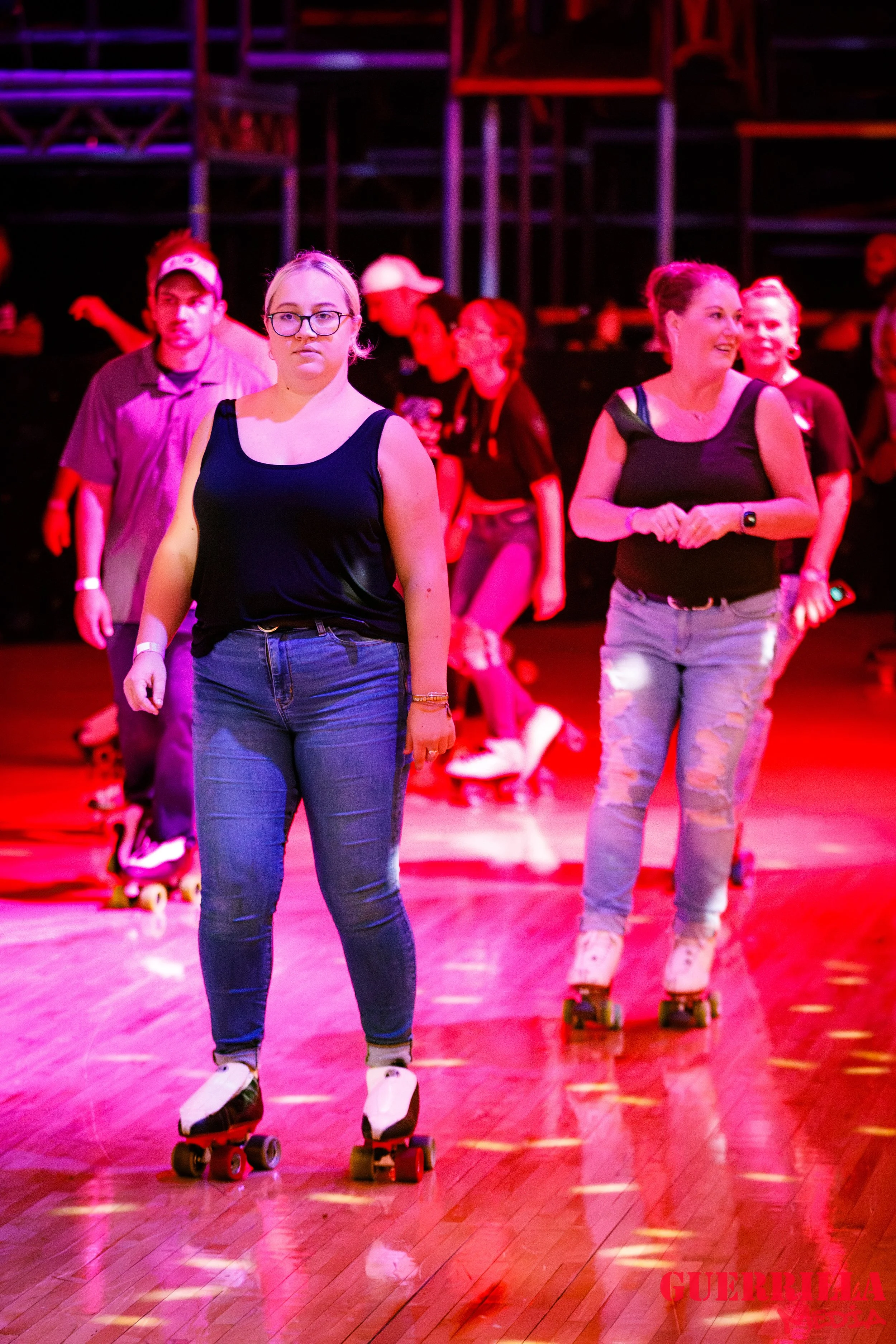 People roller skating on a wooden floor under colorful red and purple lighting.