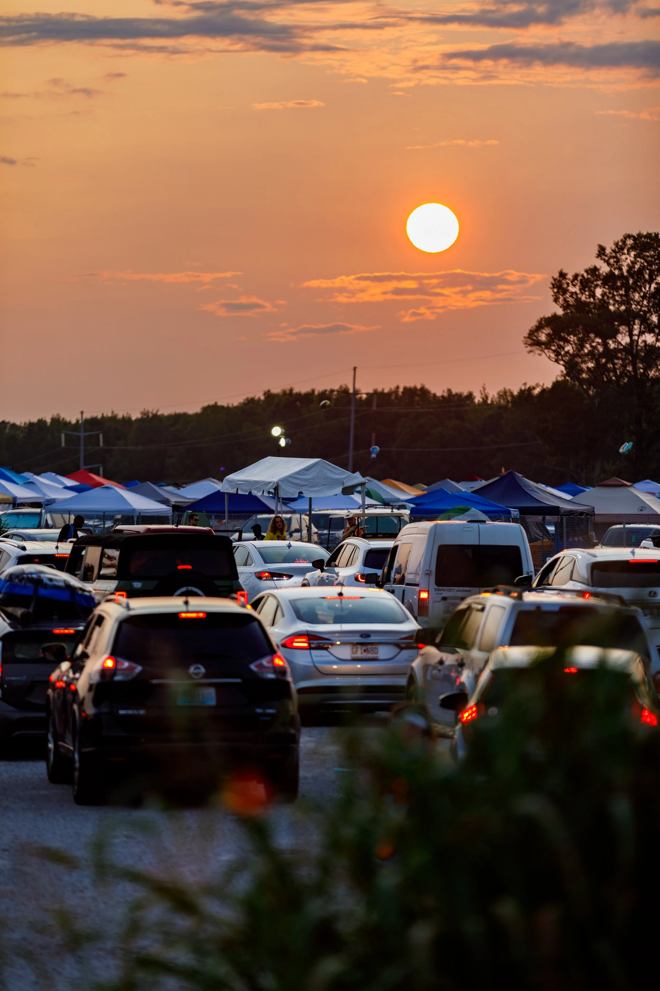 A parking lot filled with cars and tents during sunset.