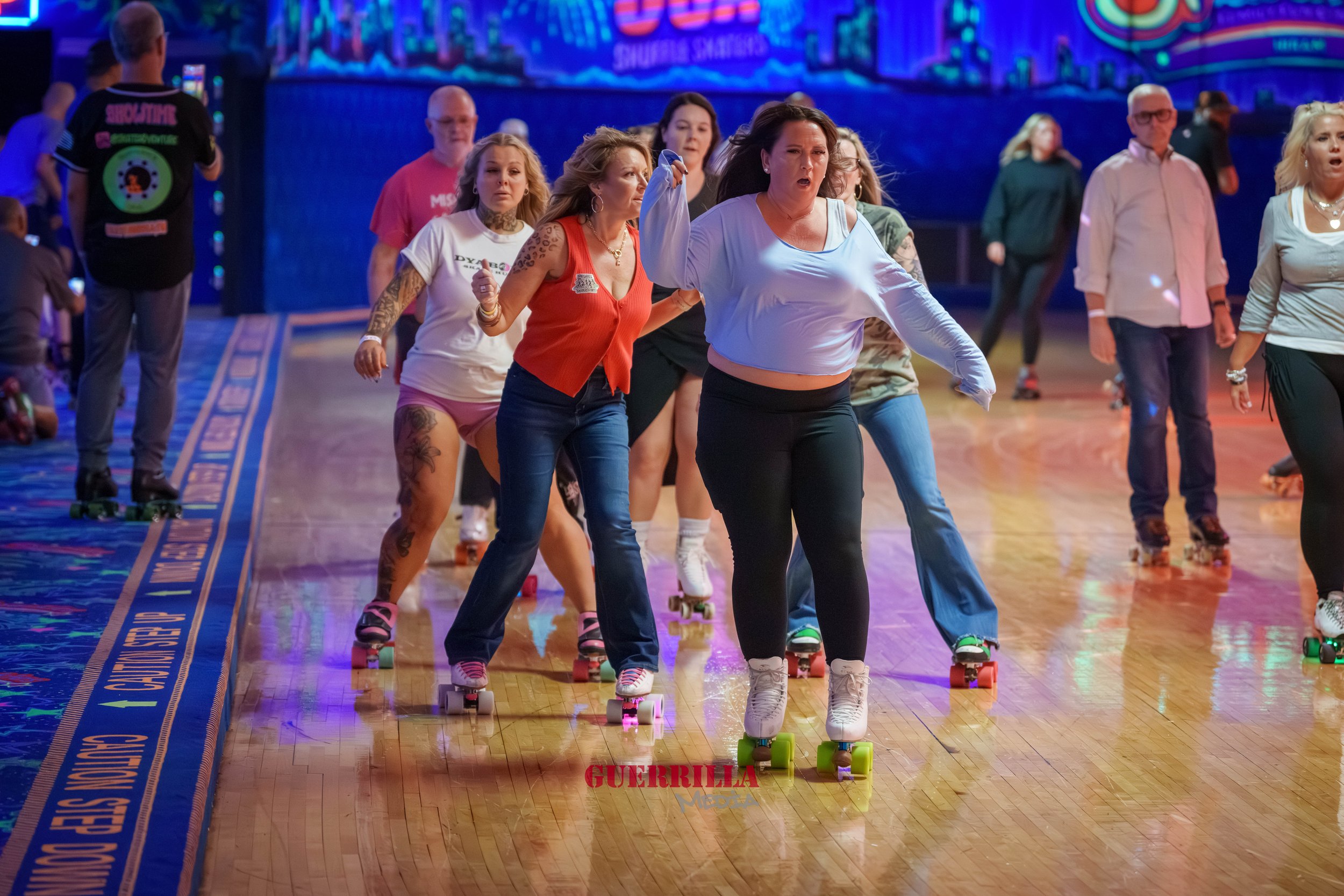 People roller skating in an indoor rink with colorful neon lights and a cityscape background.