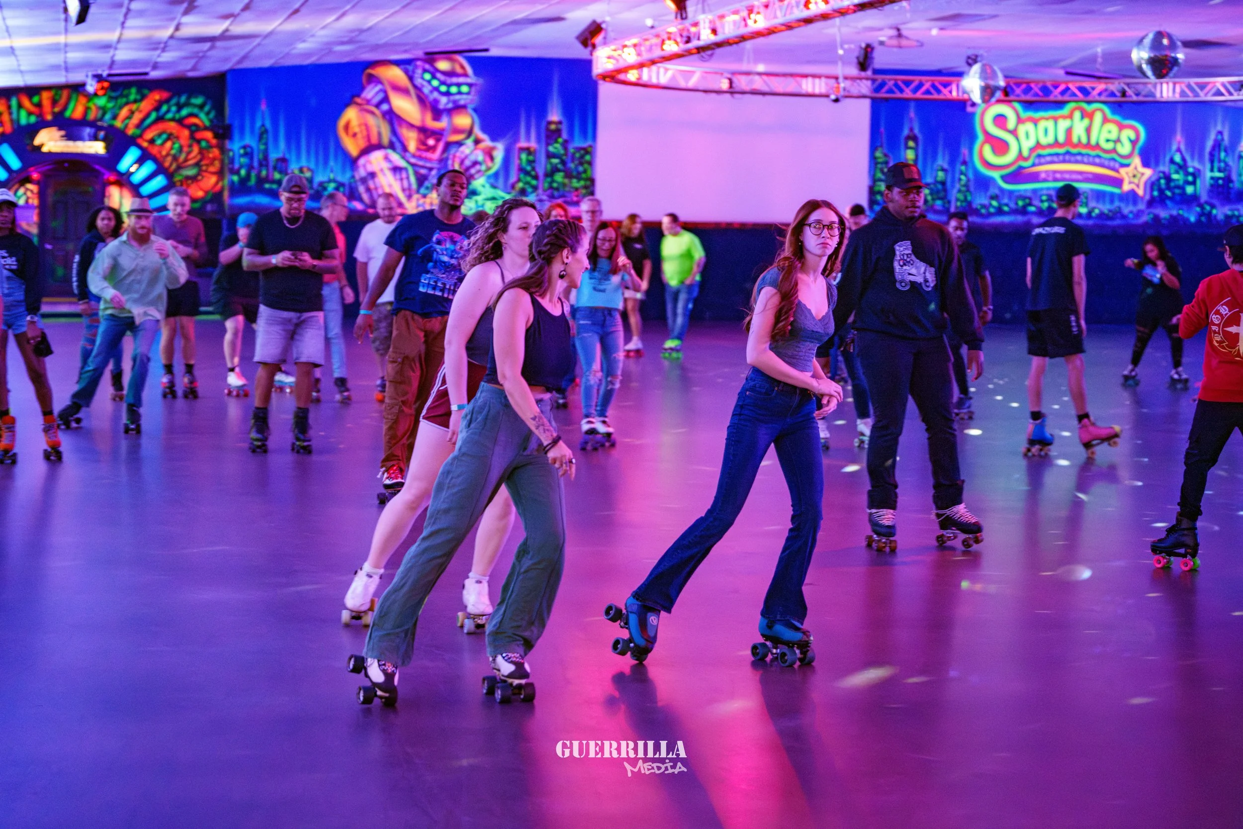 People roller skating at an indoor roller rink with colorful neon lights and graffiti-style murals on the walls.