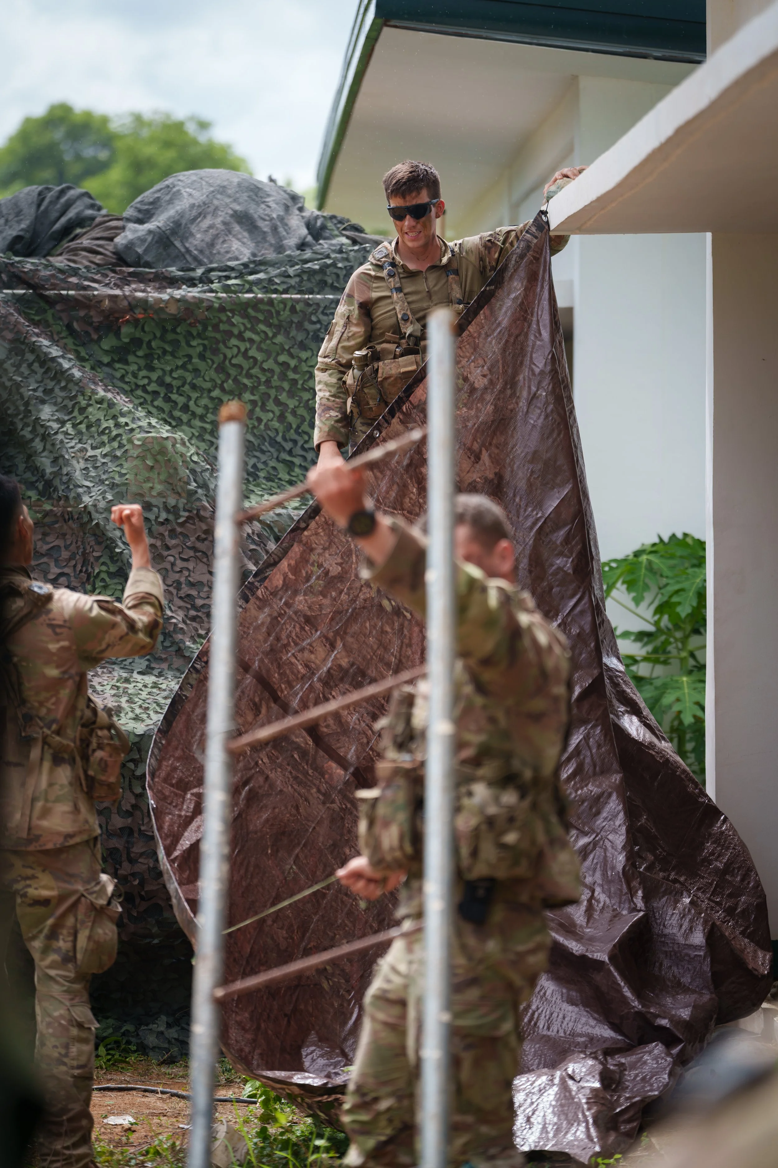 Soldiers setting up a camouflage net outside a building.
