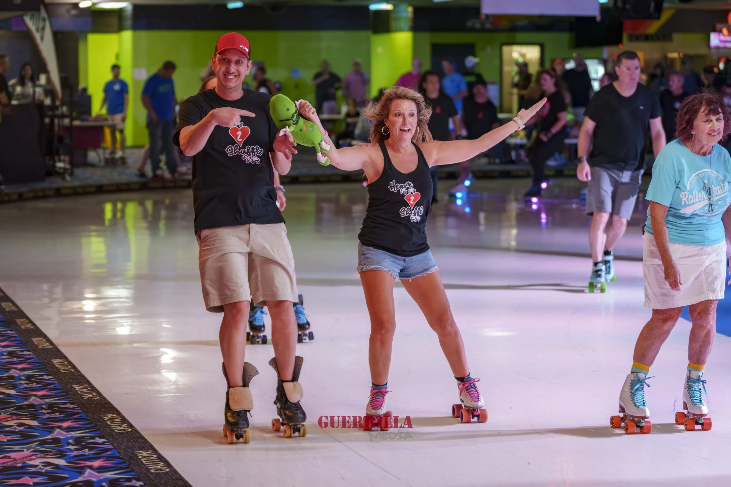 People roller skating indoors, including a man pointing at a woman holding an inflatable green octopus, wearing casual clothes and roller skates, in a lively atmosphere.