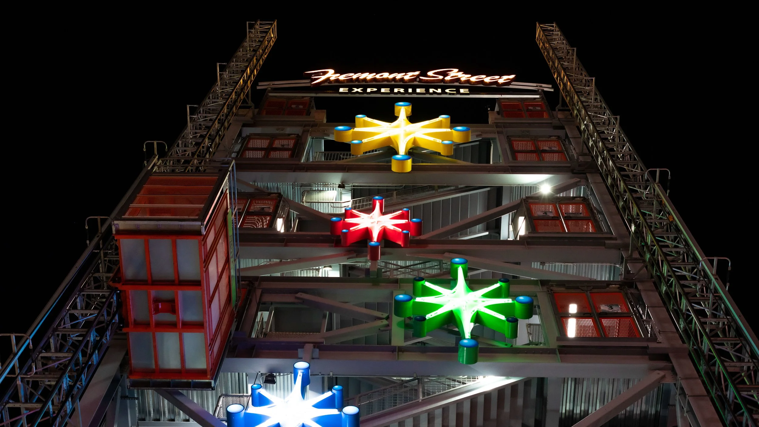Night view of a Ferris wheel with illuminated candy cane shaped lights in red, green, and blue, and a sign at the top that reads 'Premium Street Experience'.