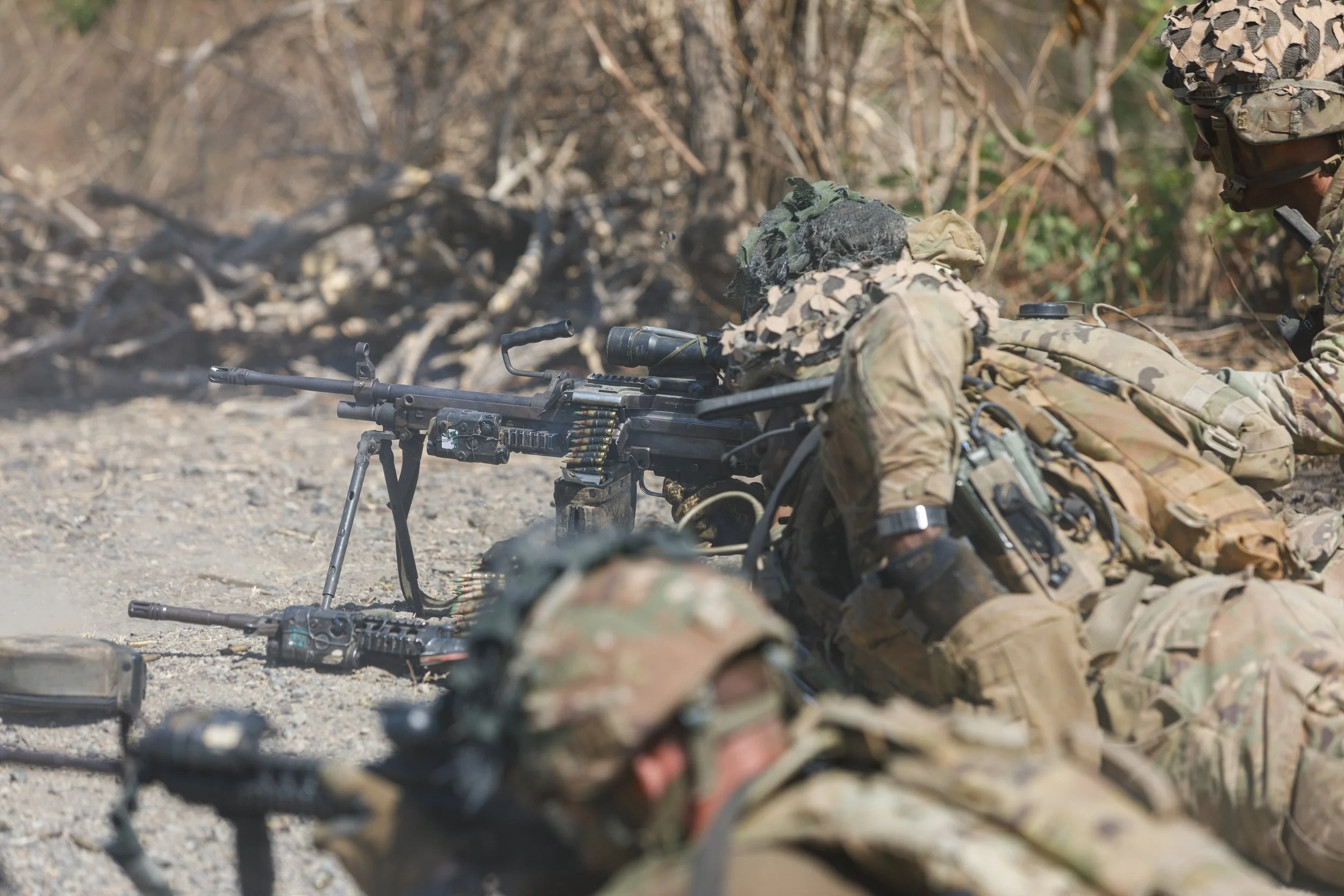 Military soldiers lying on the ground with a mounted machine gun during a combat training or war scene.