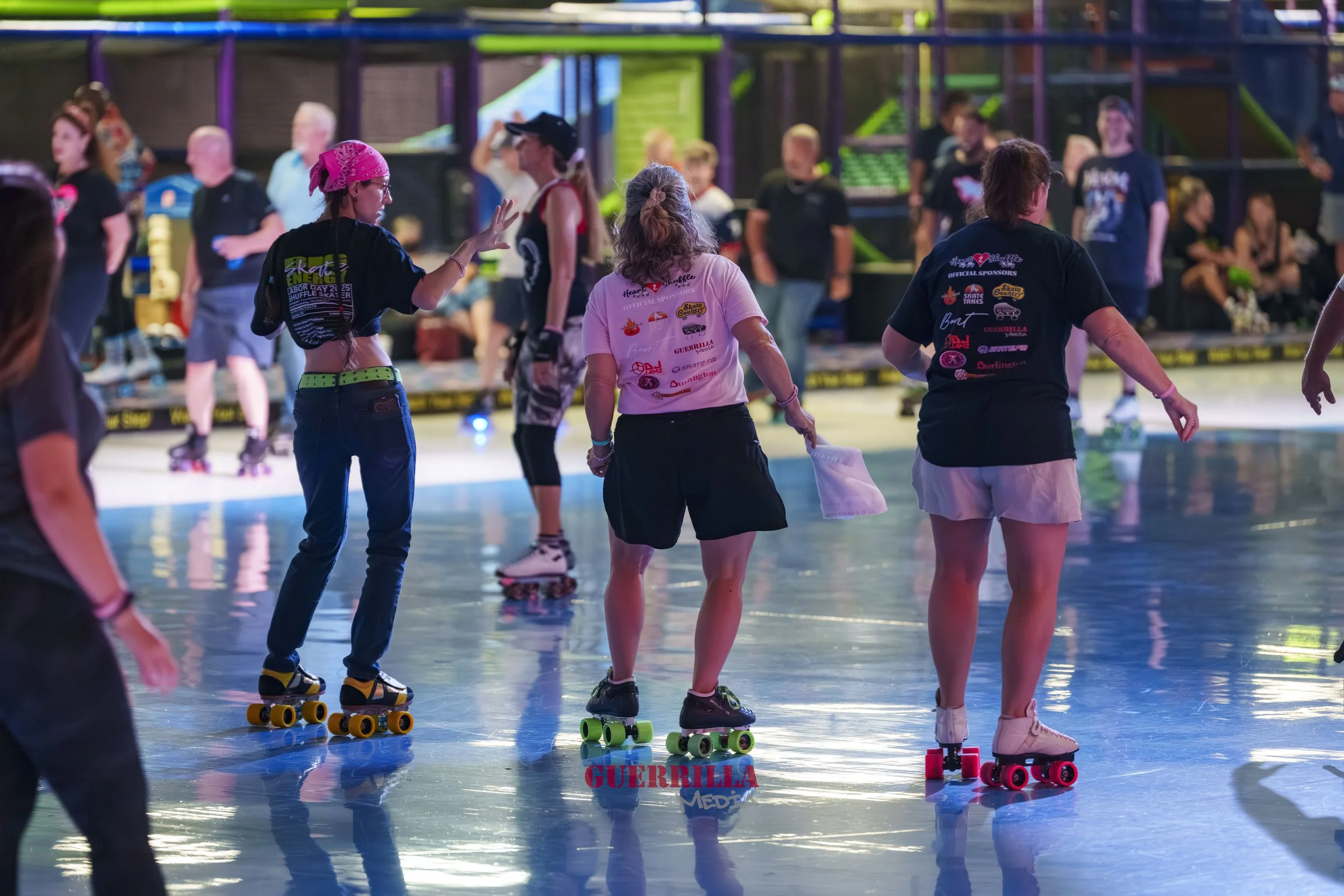 People roller skating inside an indoor skating rink with colorful lights and spectators in the background.