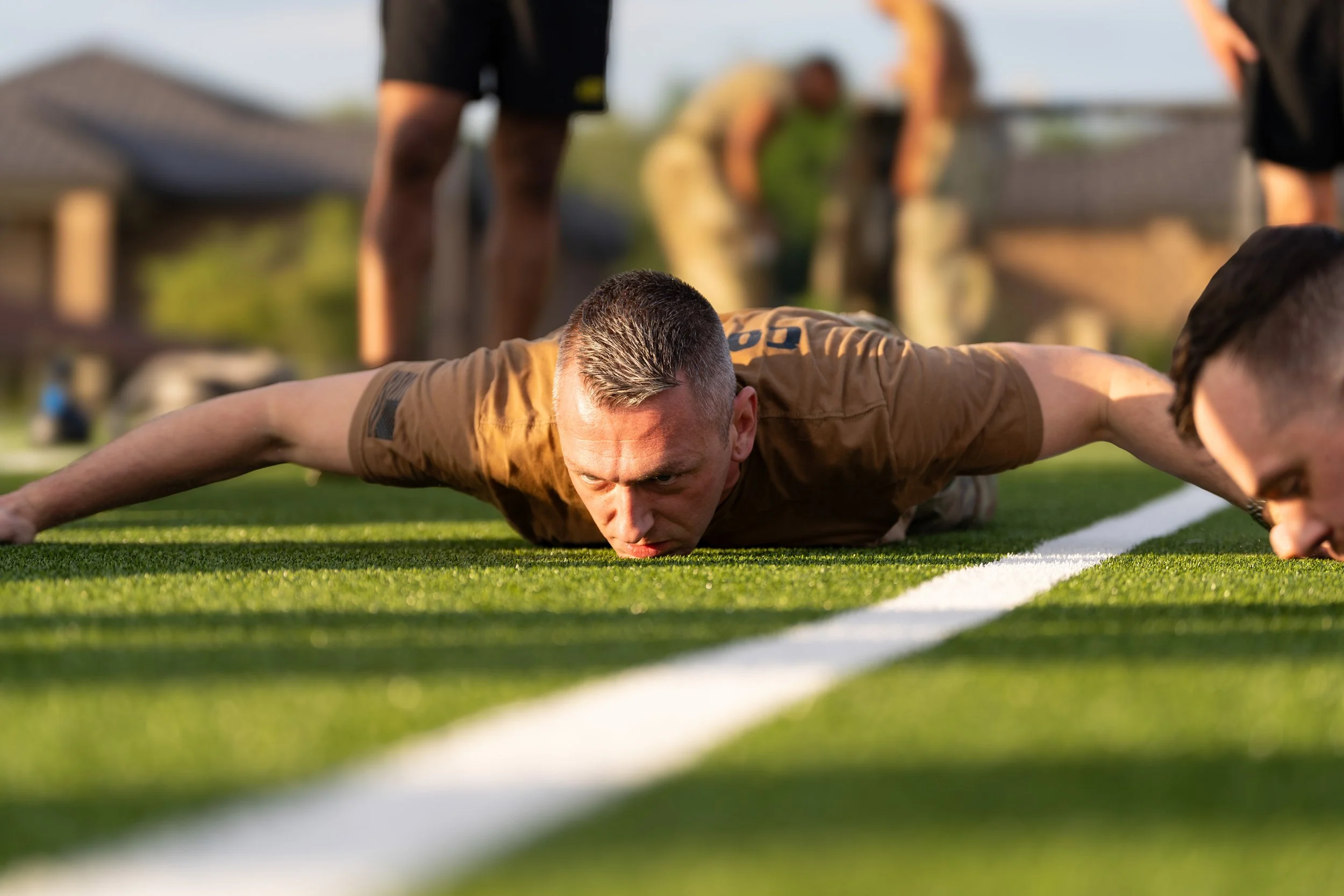 A man laying face down on a football field with his arms extended, during a training or exercise session.