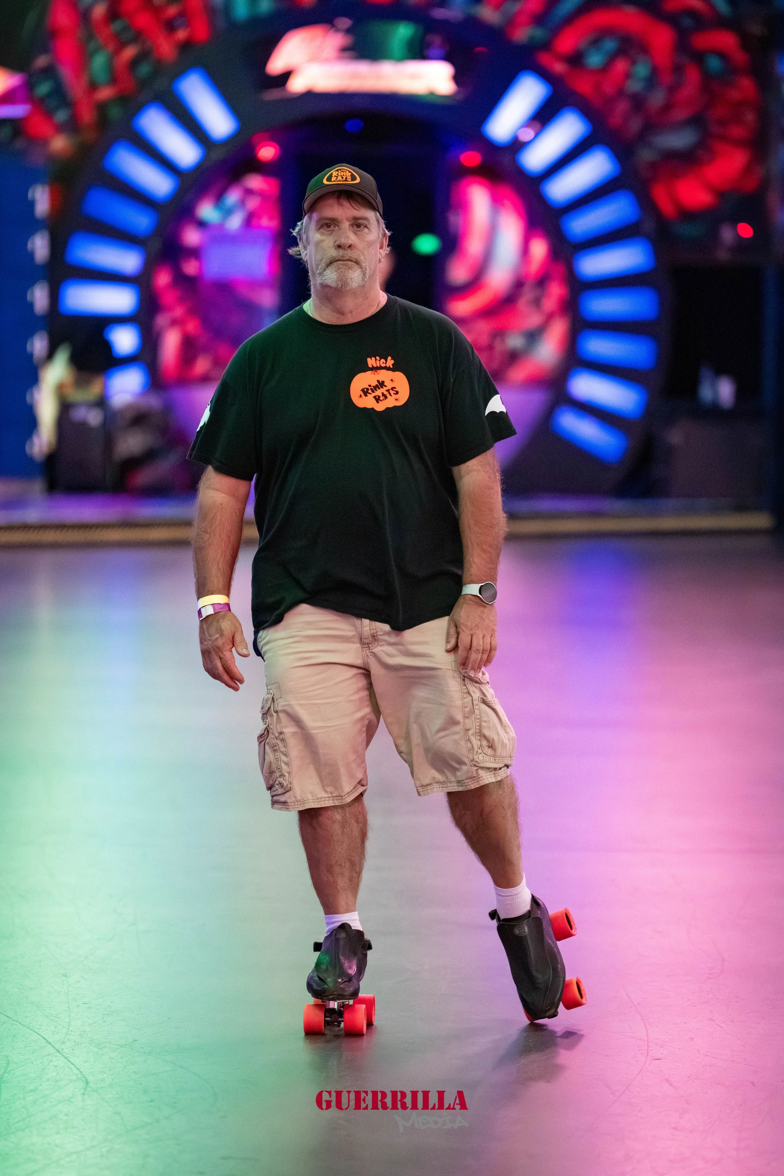 A middle-aged man with a beard skating indoors at an arcade or entertainment center, with colorful neon lights and a futuristic background.