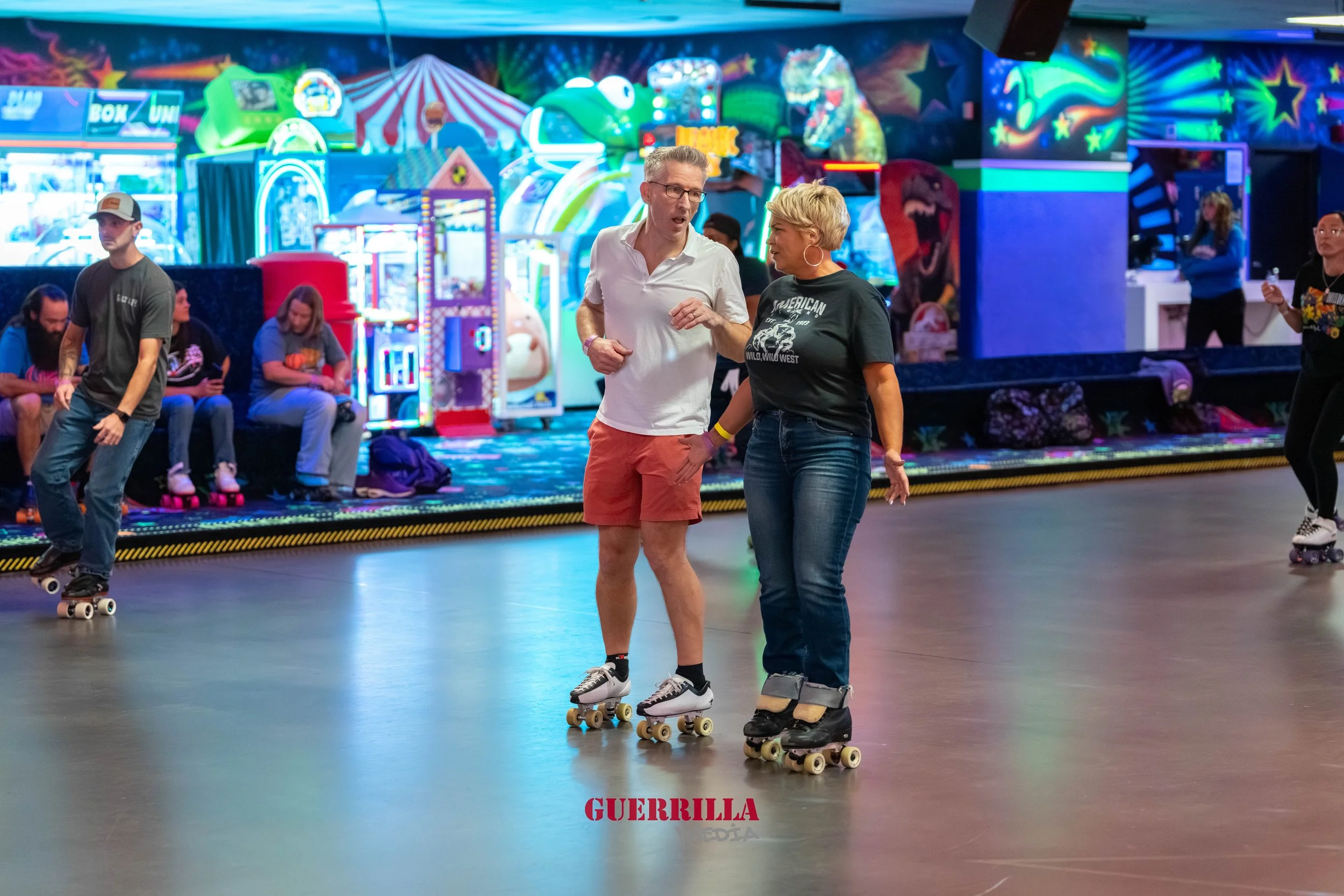 People roller skating in an indoor roller rink decorated with colorful neon lights and arcade games.