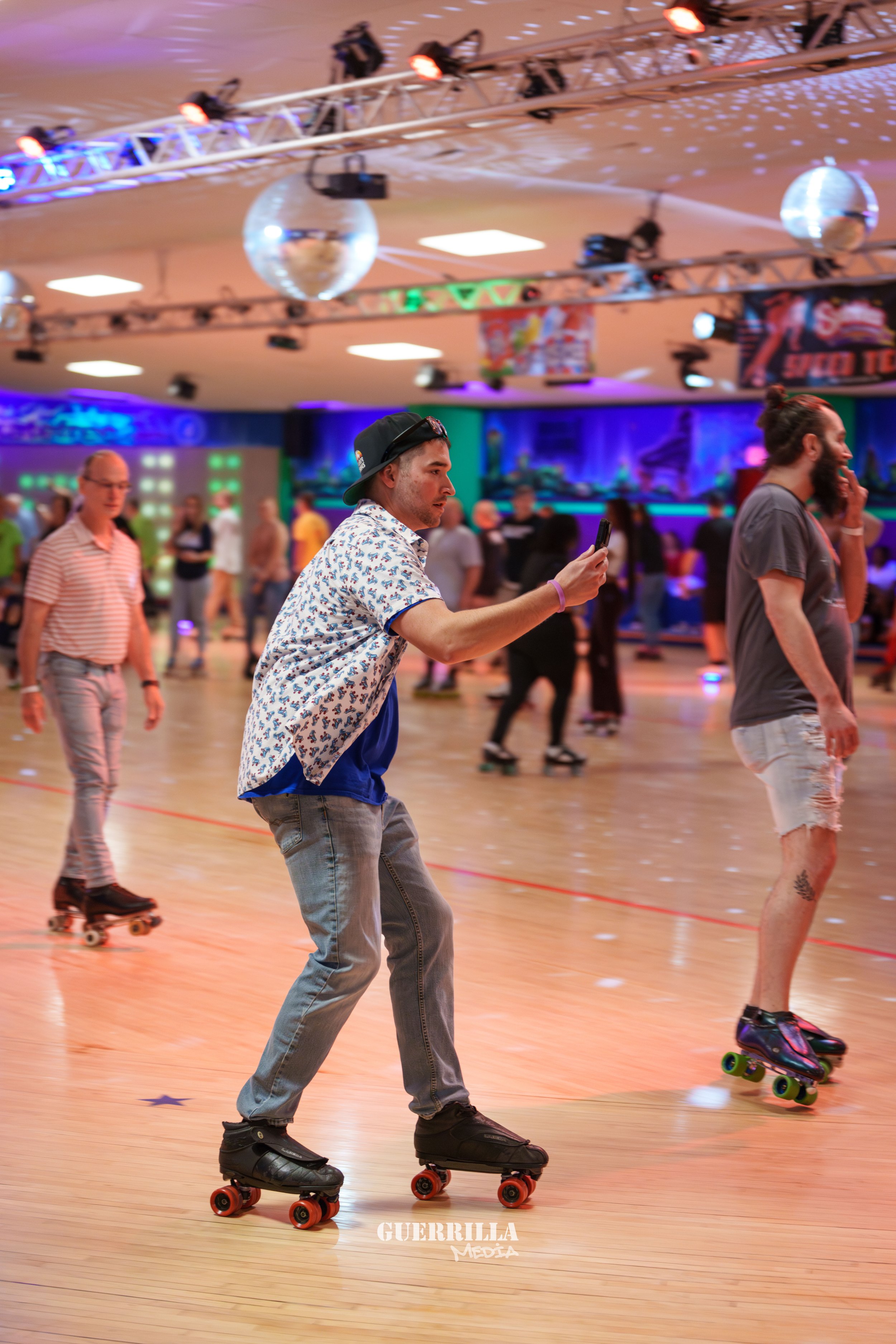 People roller skating in an indoor roller rink with colorful lighting and disco balls.