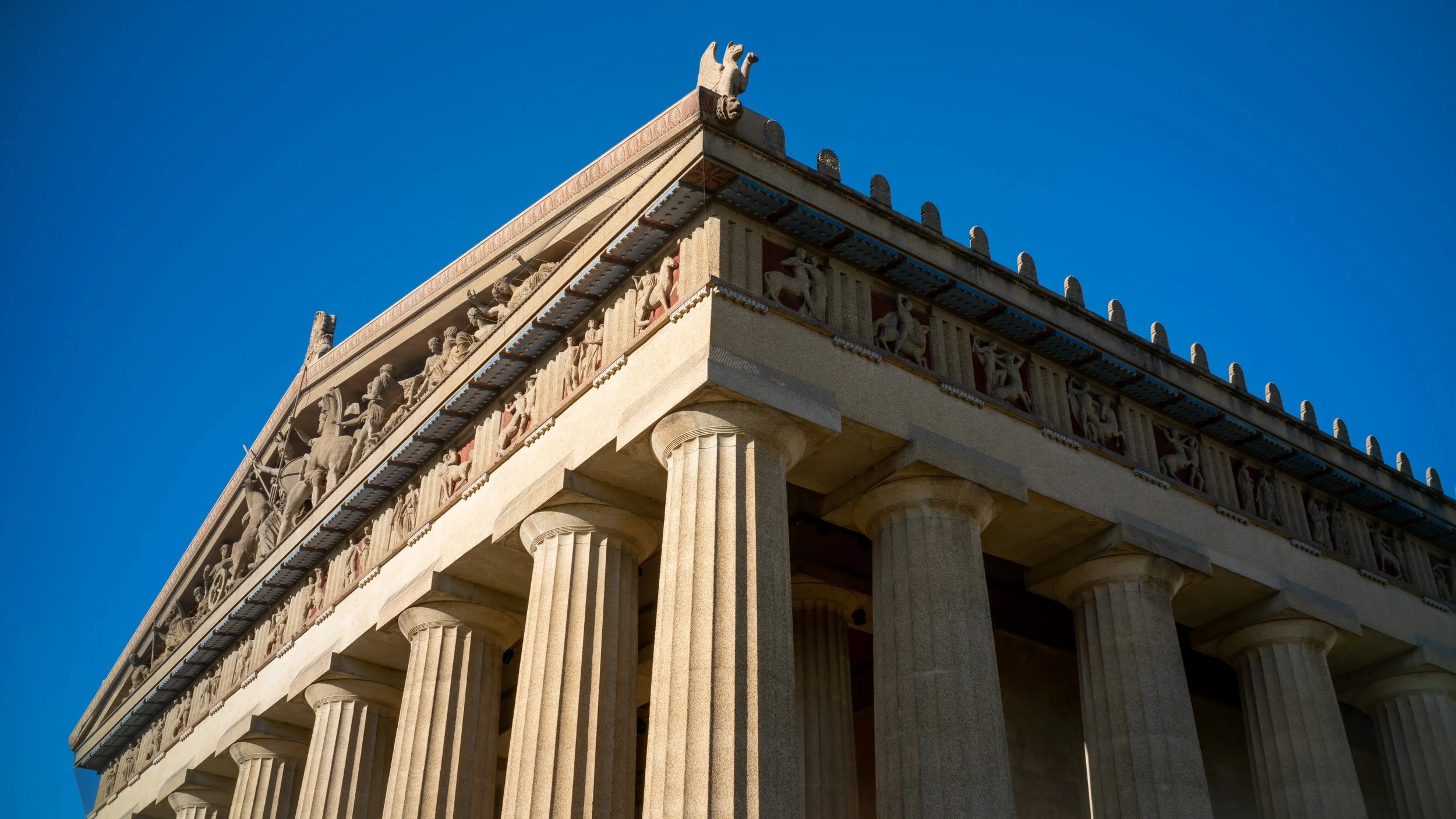 Close-up of the Parthenon in Athens, Greece, with tall Doric columns and intricate friezes under a clear blue sky.