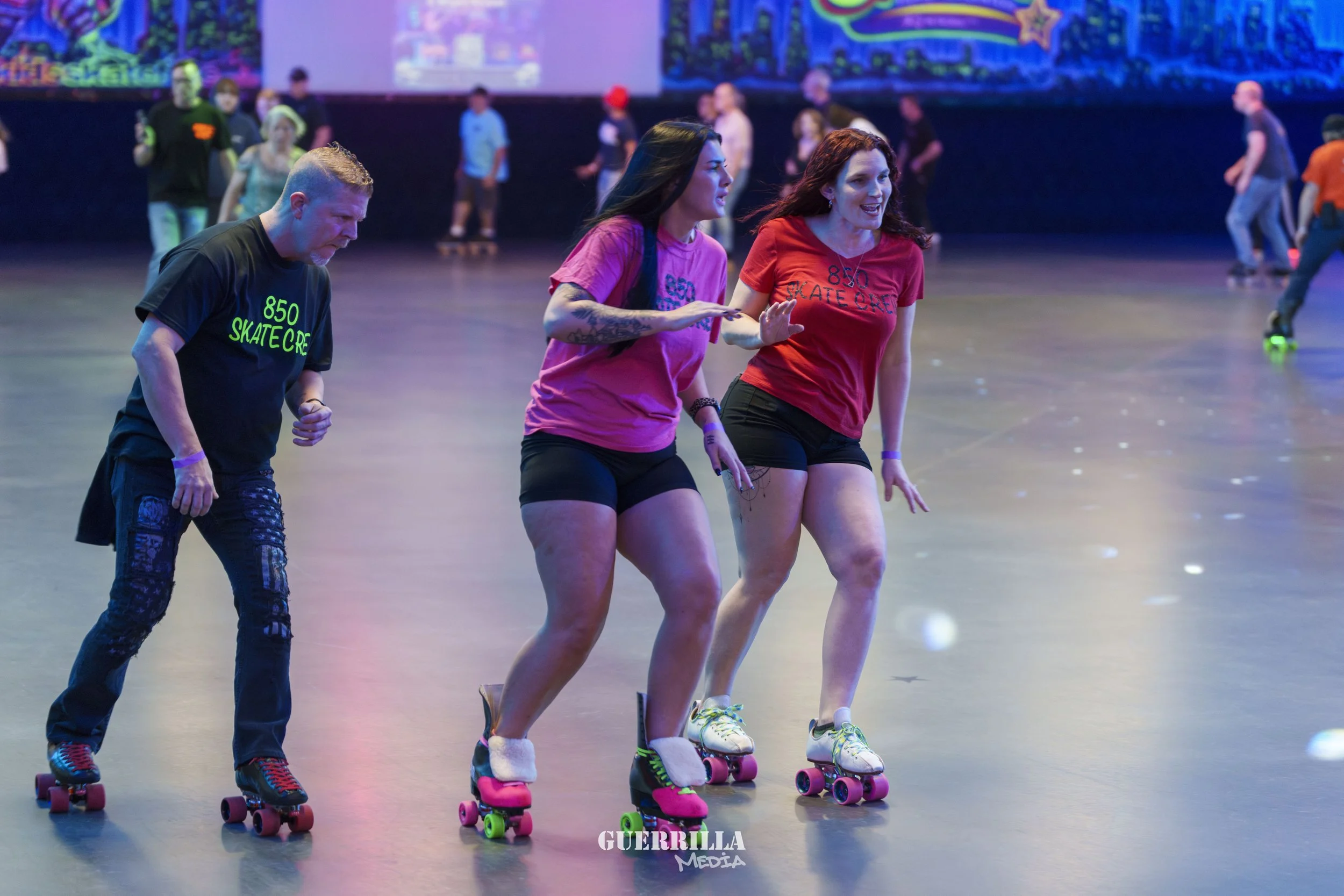 People roller skating at an indoor roller rink, with some wearing matching t-shirts and different colored skates.