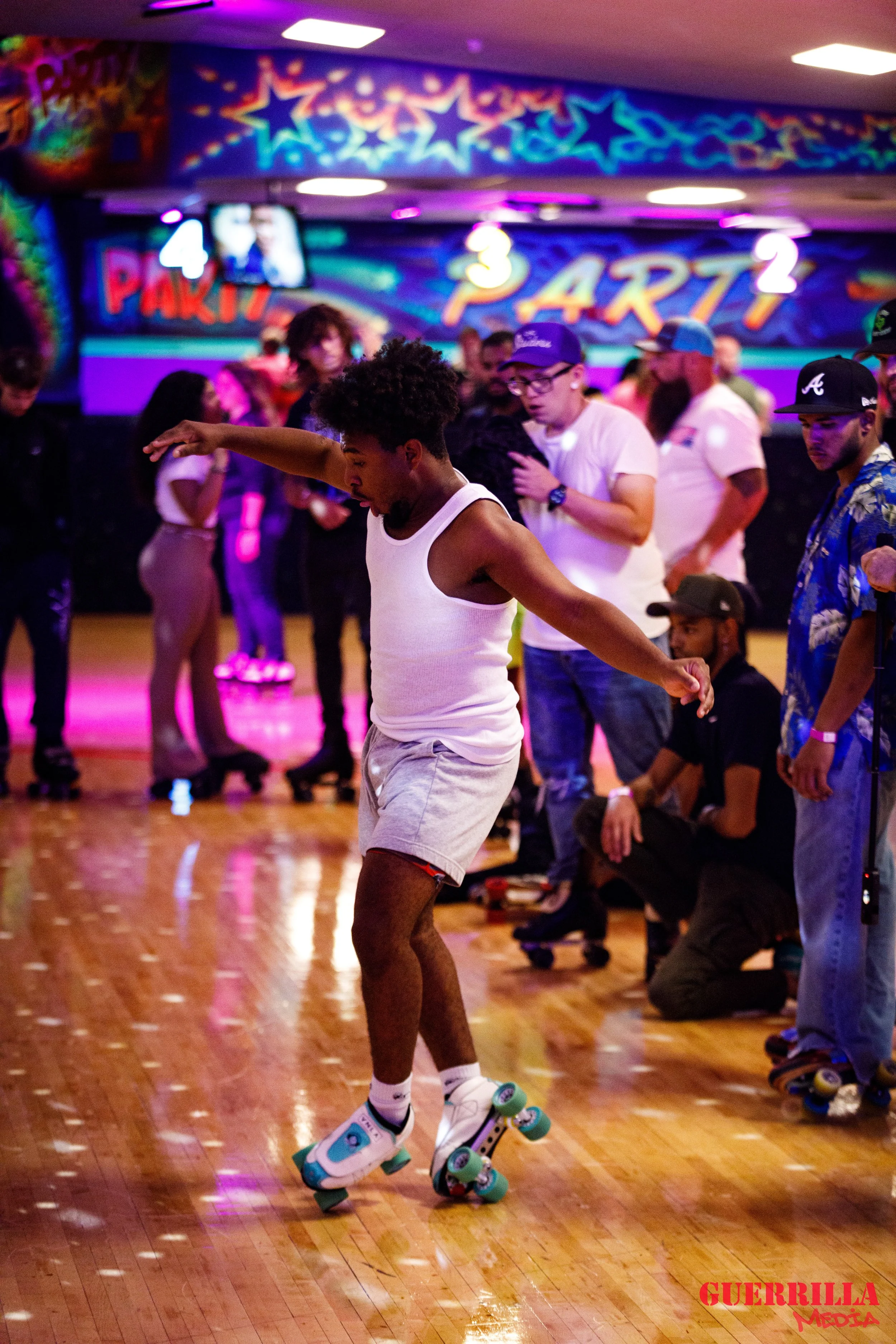 A young boy roller skating indoors at a roller rink with colorful neon lights and people in the background.