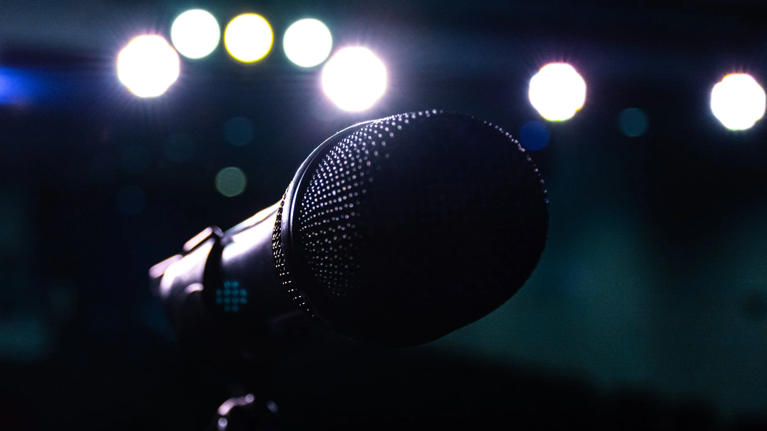 Close-up of a microphone on a dark stage with colorful, blurred lights in the background.