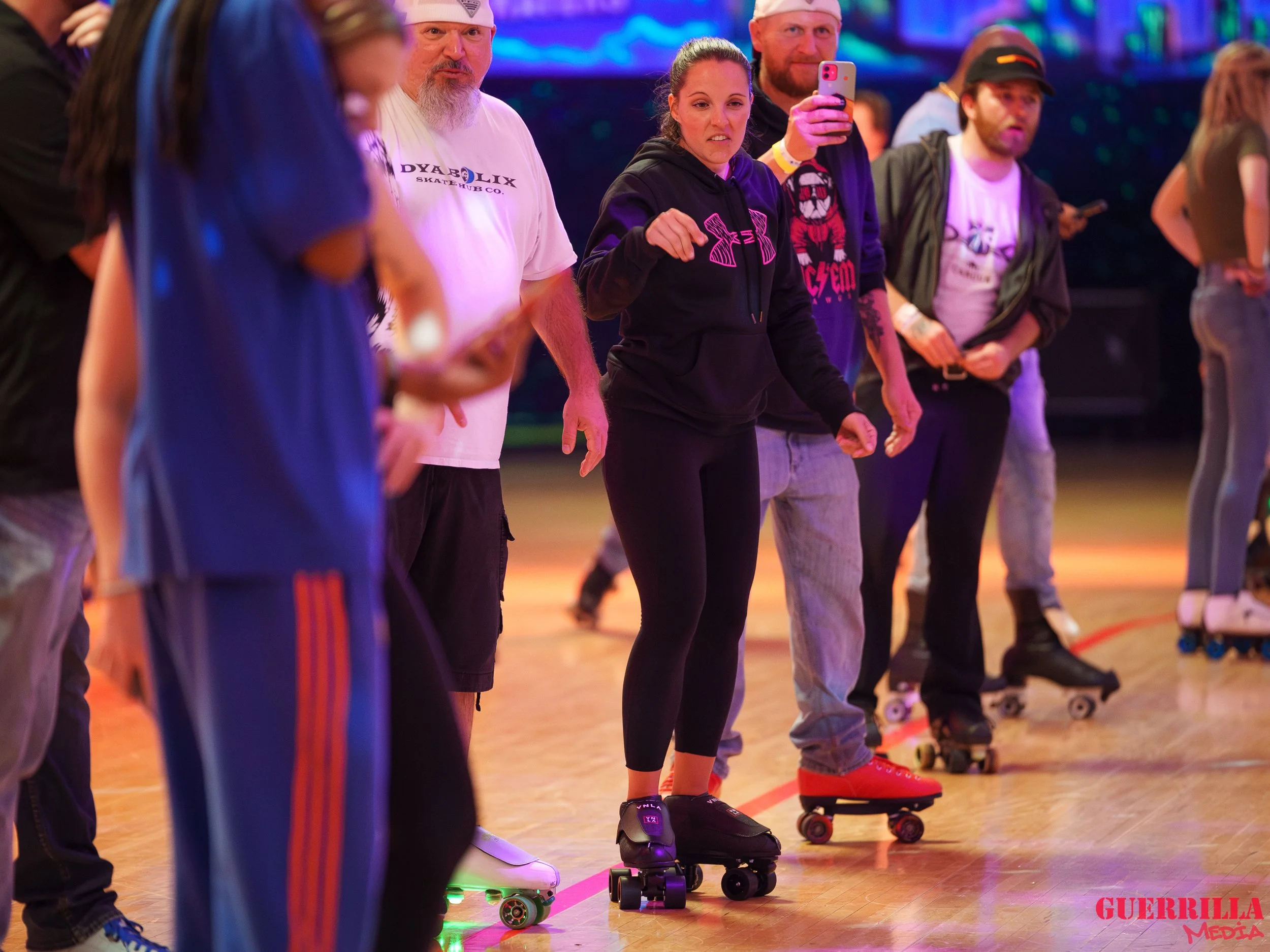 Group of people participating in roller skating at an indoor rink with colorful lighting.
