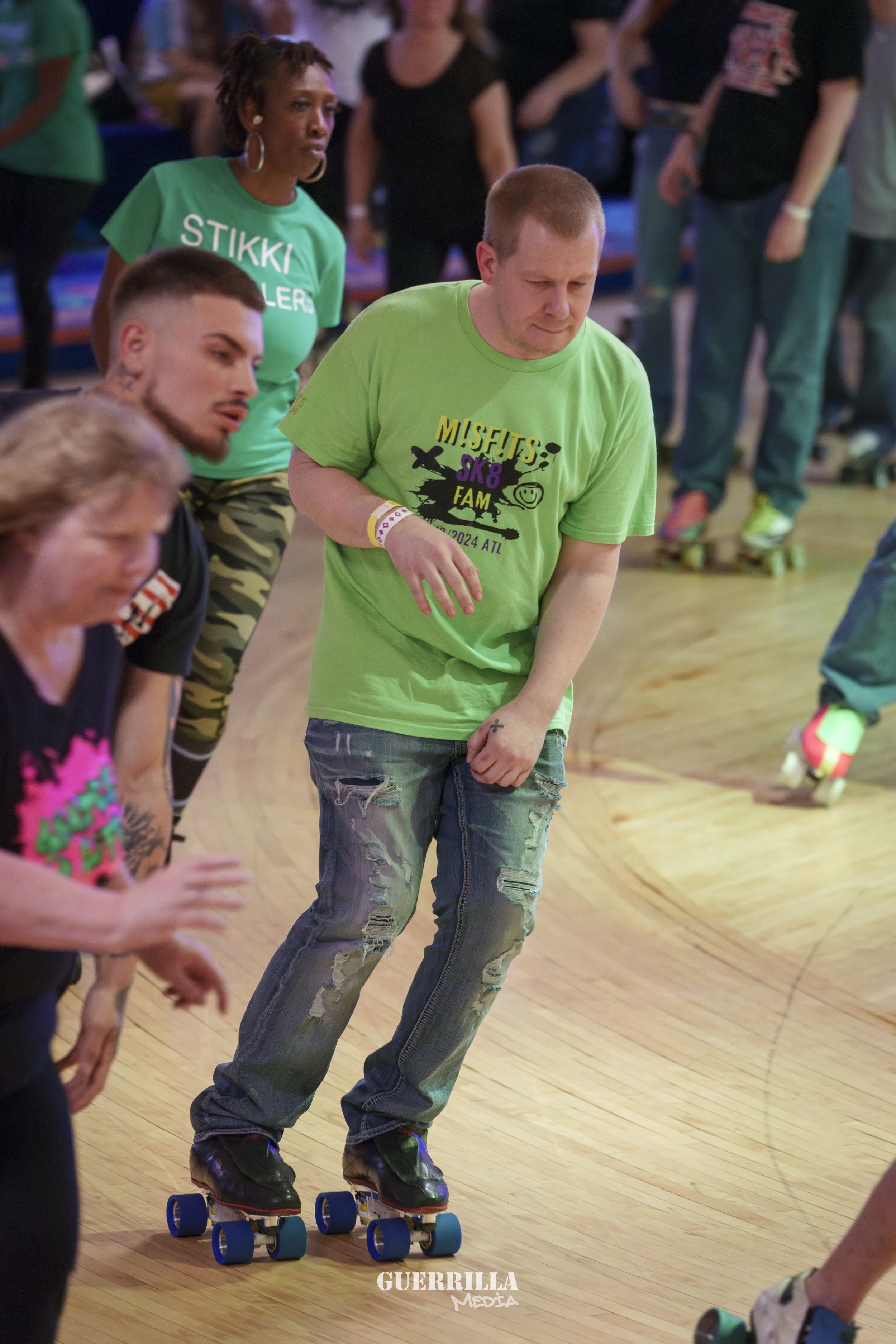 People roller skating indoors, some wearing casual clothing and wristbands, on a wooden floor at a social event.