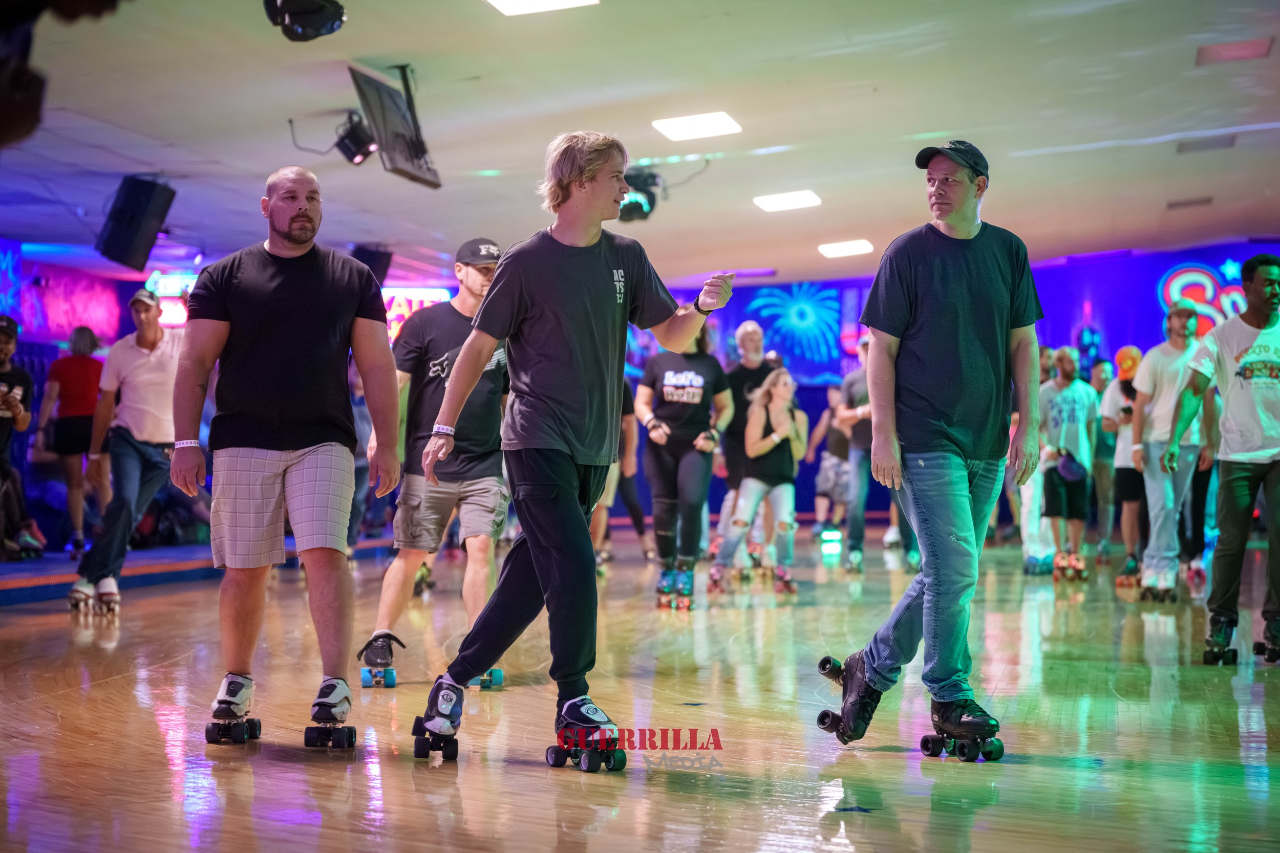People roller skating inside a roller rink with colorful neon lights and decor in the background.