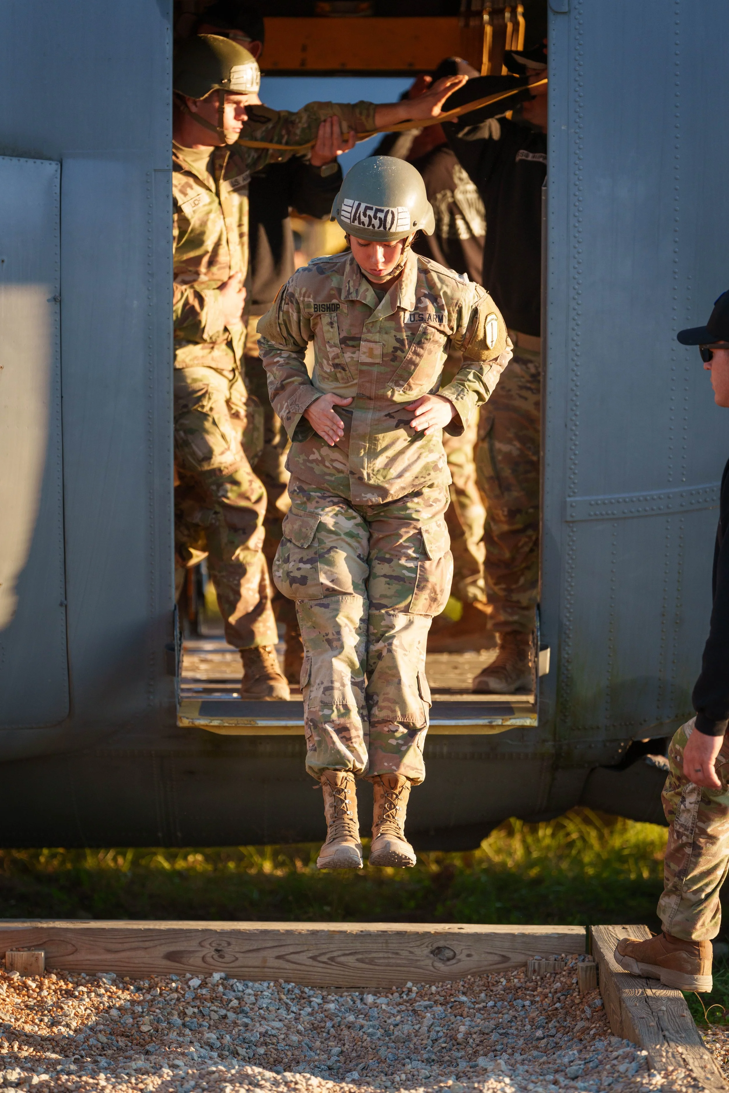 A female soldier in camouflage uniform and helmet is stepping out of a military helicopter during a training exercise.