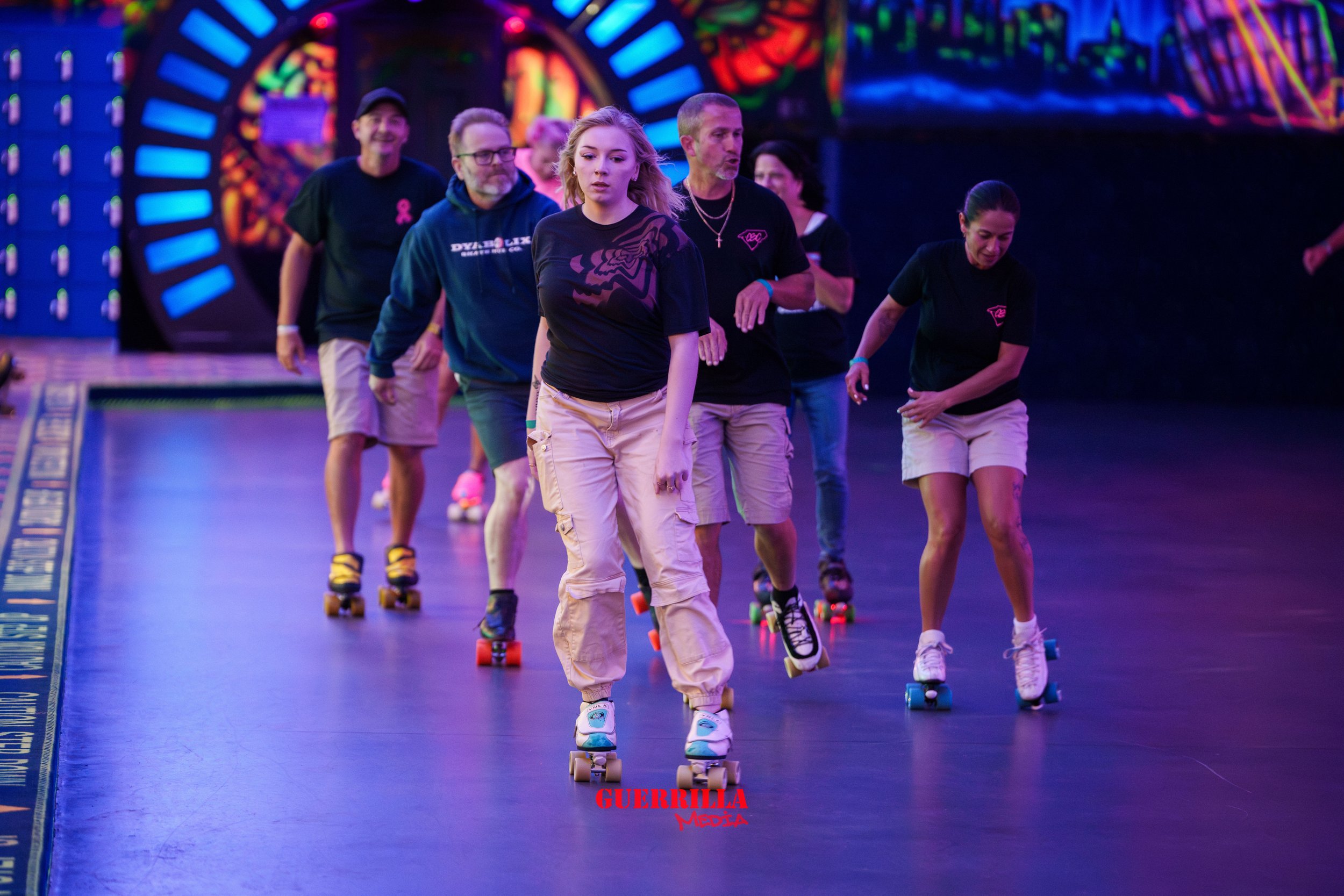 Group of people roller skating in an indoor skate rink with colorful, neon-lit background.