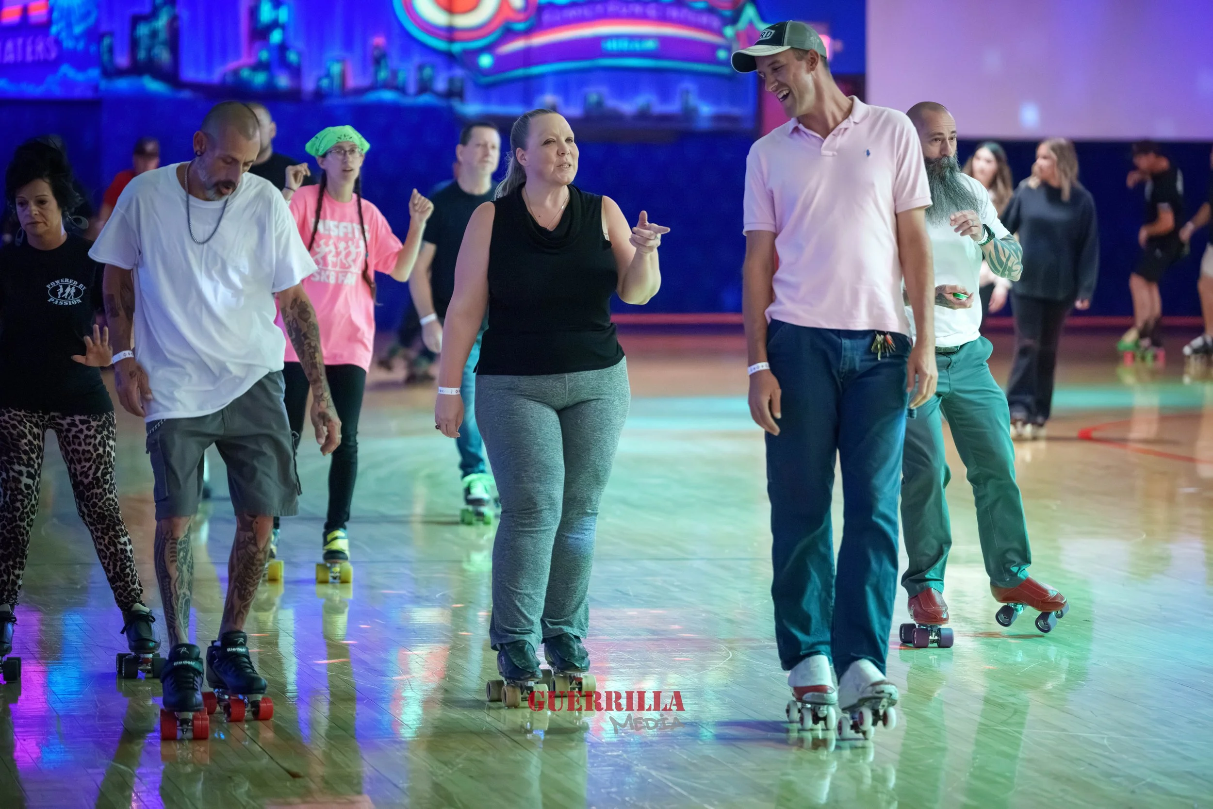 People roller skating at an indoor rink with colorful lights in the background.