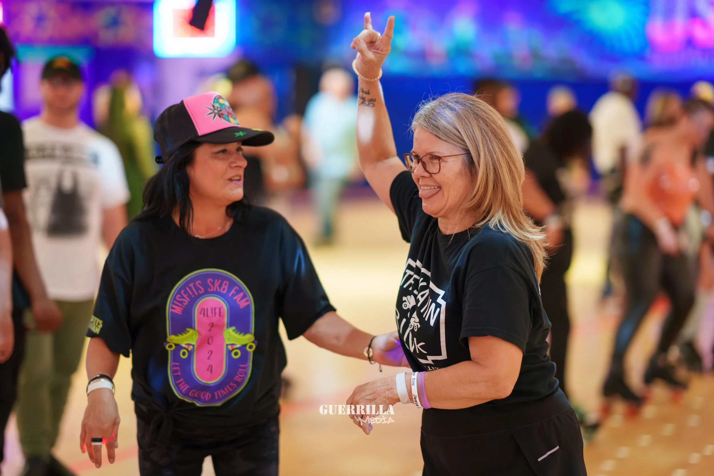 Two women dancing and enjoying themselves at a roller skating rink, with other skaters in the background.