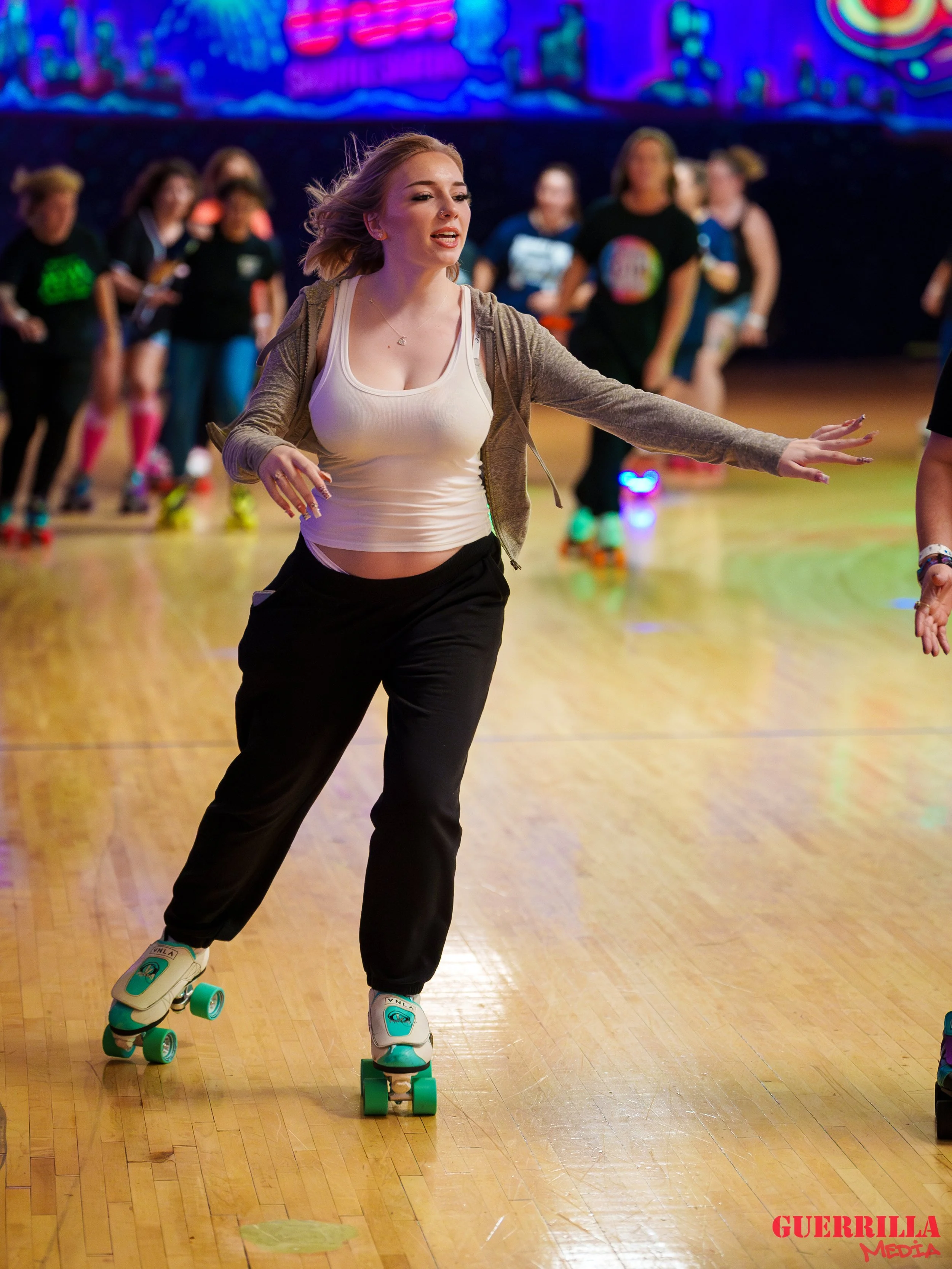 A woman roller skating indoors at a roller rink, with other skaters blurred in the background.