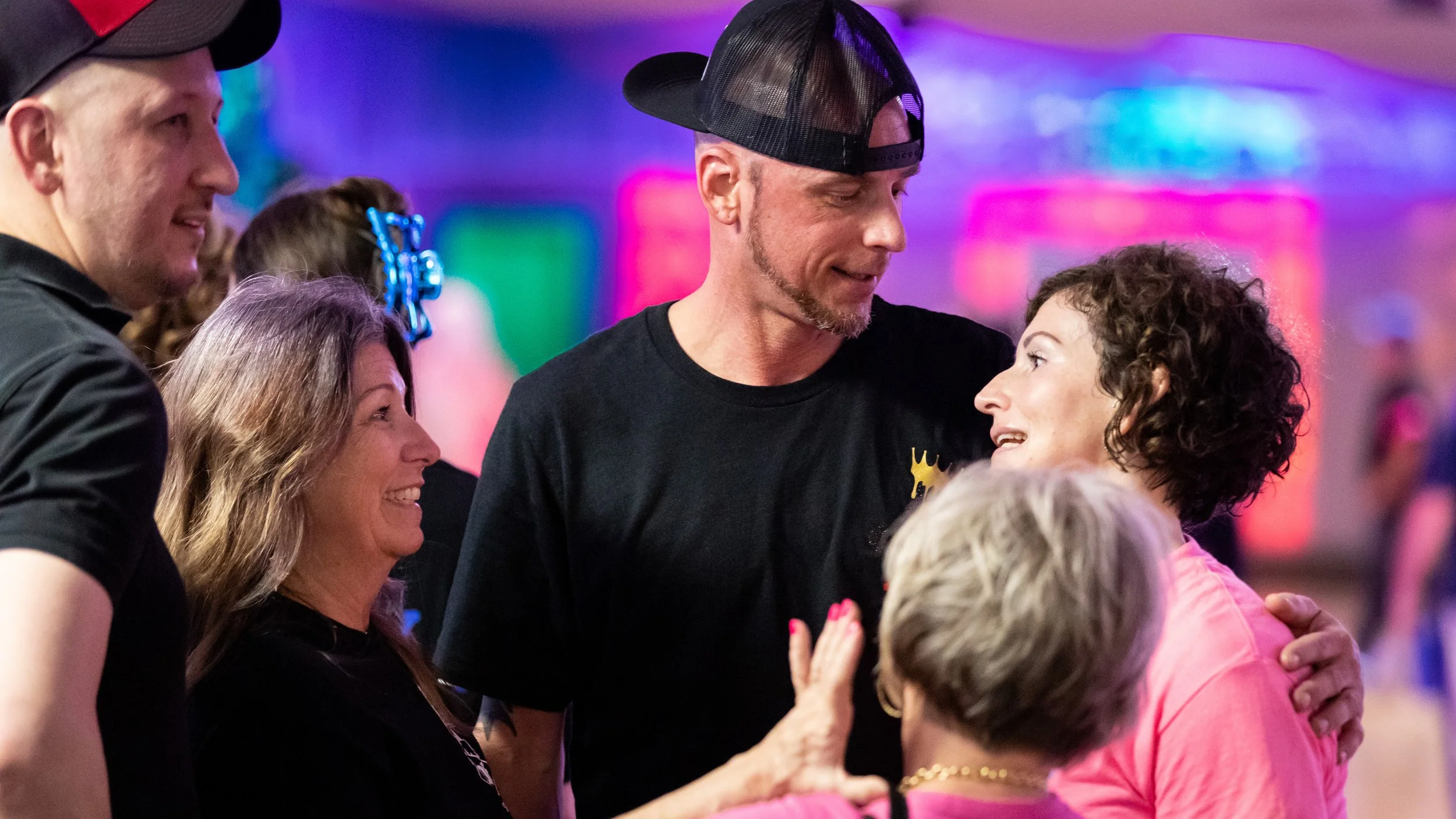 Group of people smiling and talking at a social event with colorful lights in the background.
