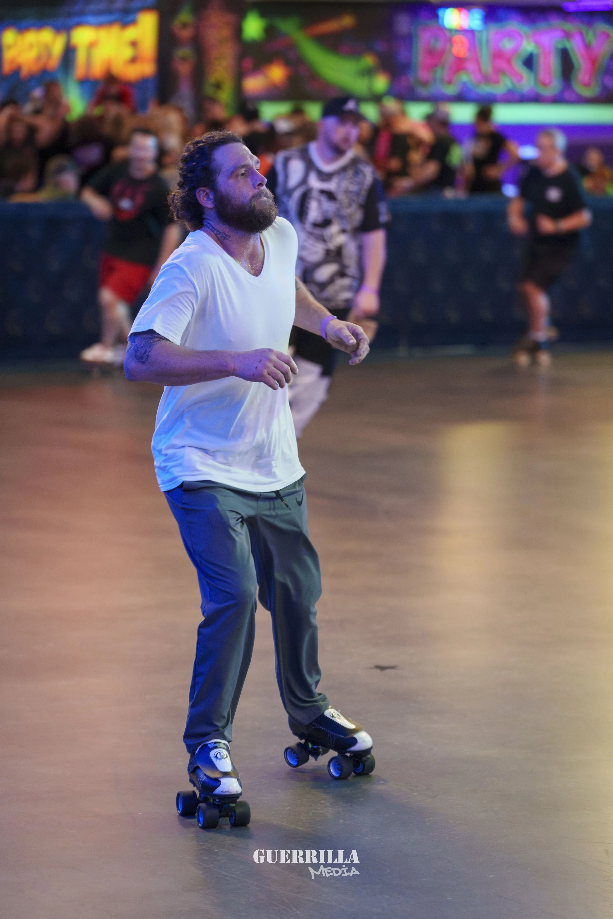 A man roller skating in an indoor roller rink with neon lights and a colorful background that reads 'Party' and 'Active Travel', with spectators in the background.