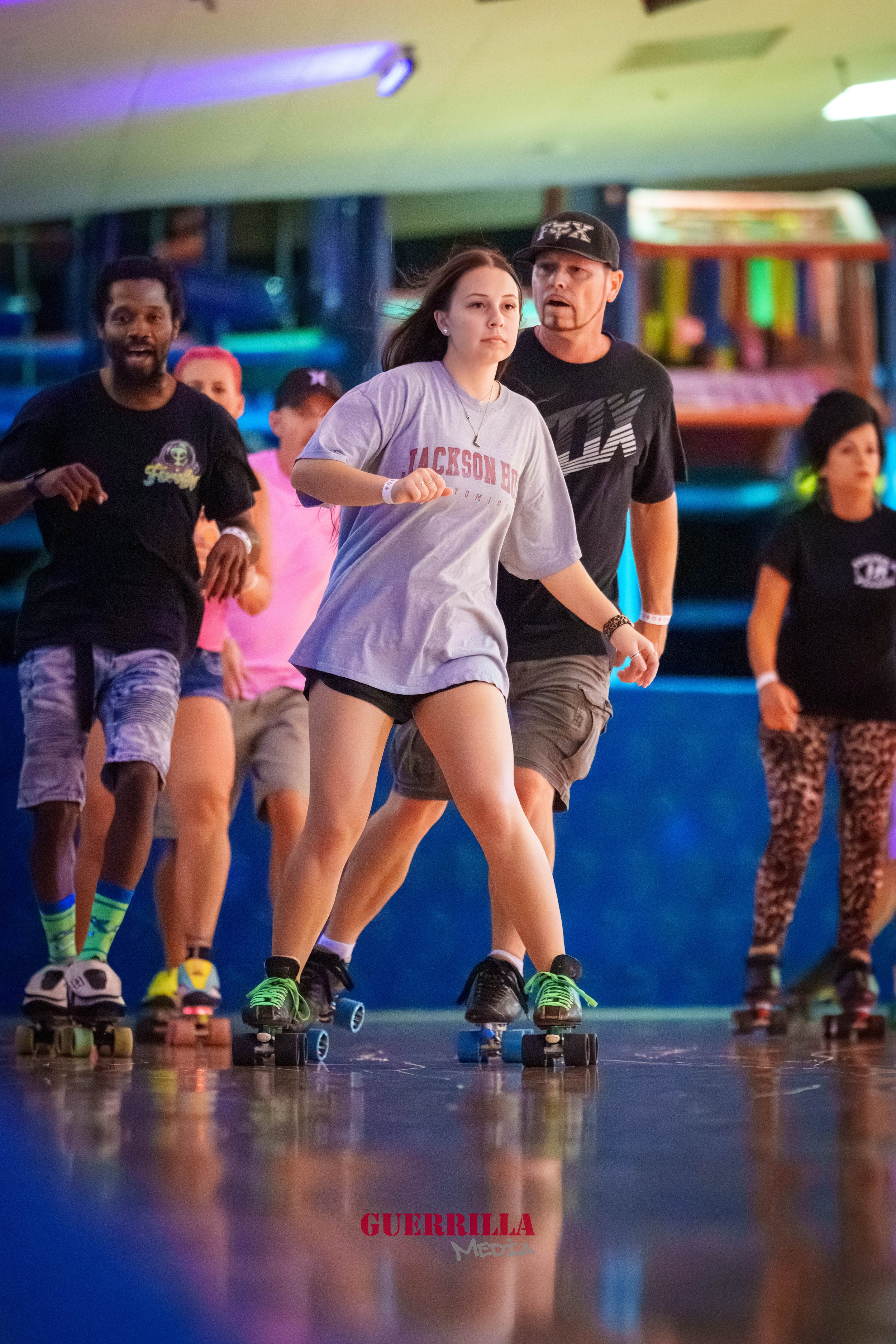 People roller skating in an indoor skating rink, some wearing casual clothes and protective gear.