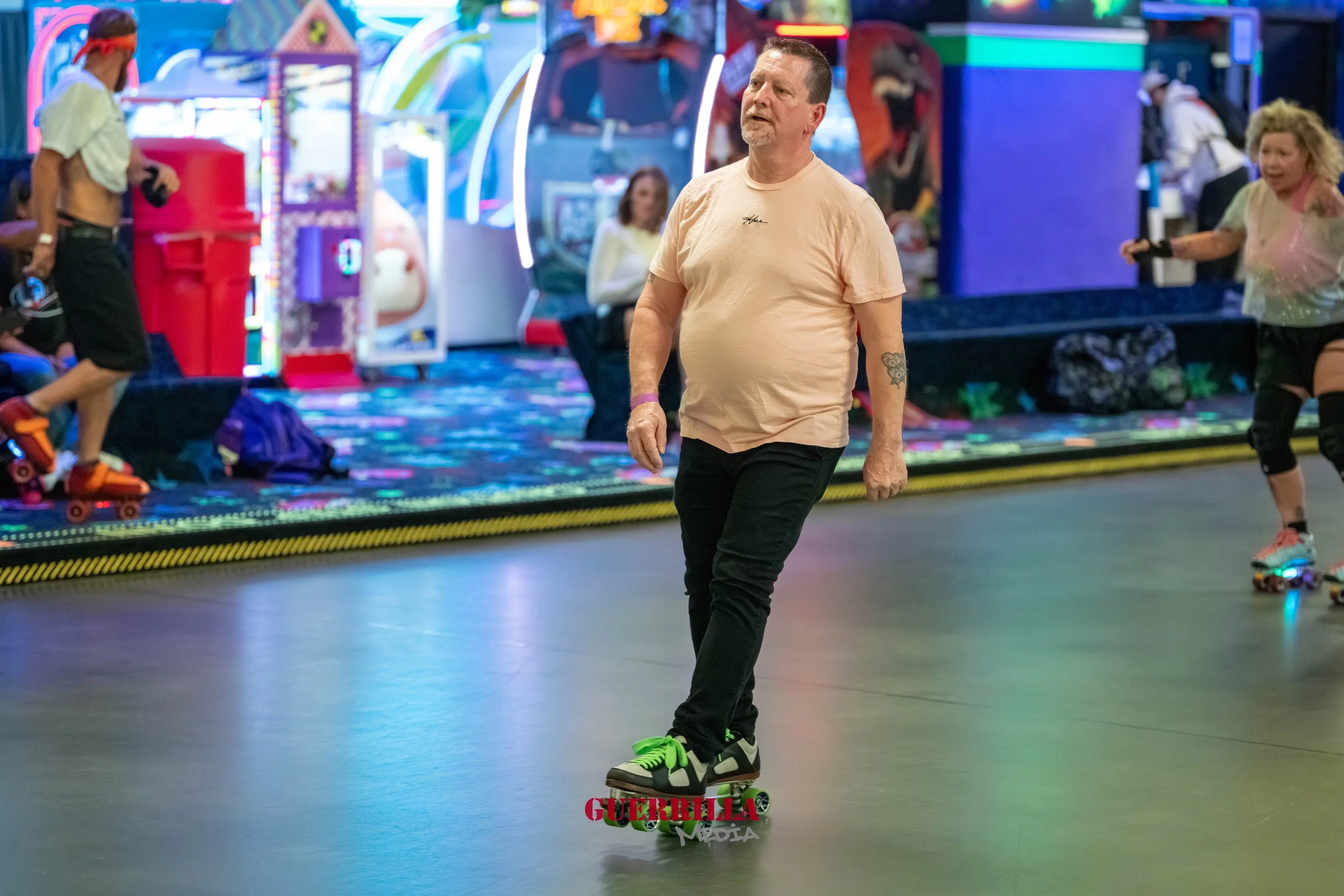 A man roller skating in an arcade or roller rink, surrounded by colorful arcade games and other skaters.
