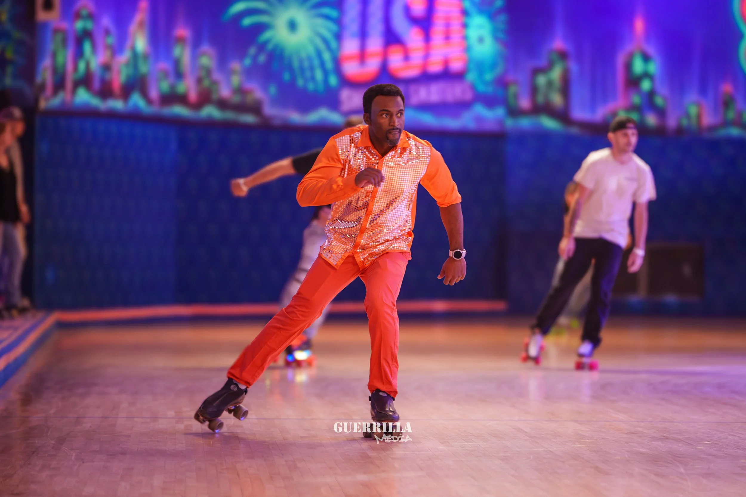 A man roller skating in an indoor rink, wearing an orange patterned shirt and orange pants, with a cityscape and fireworks display on the digital background.