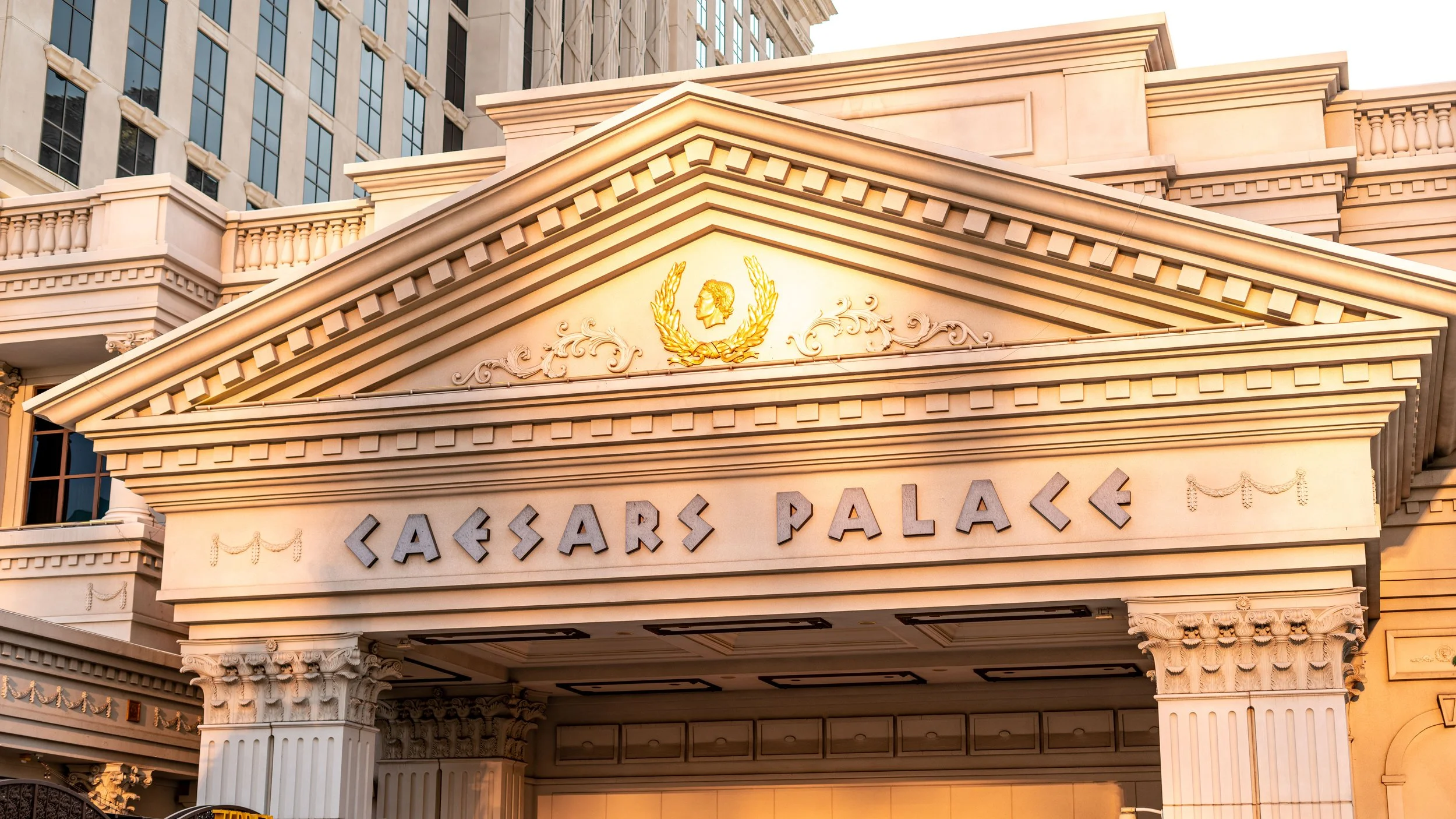 Facade of Caesars Palace with architectural details and a golden emblem of a woman's profile surrounded by laurel leaves.