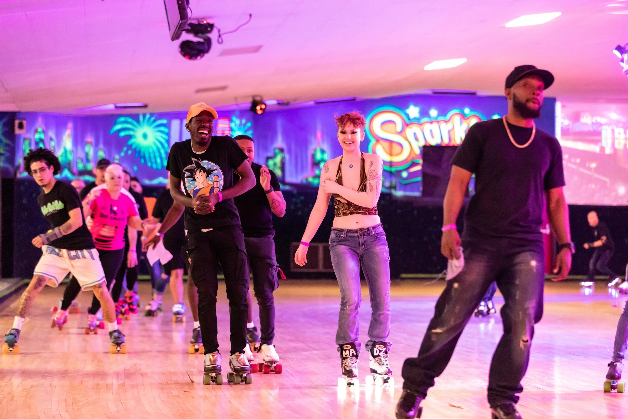 People roller skating at an indoor rink with neon lights and a colorful backdrop.