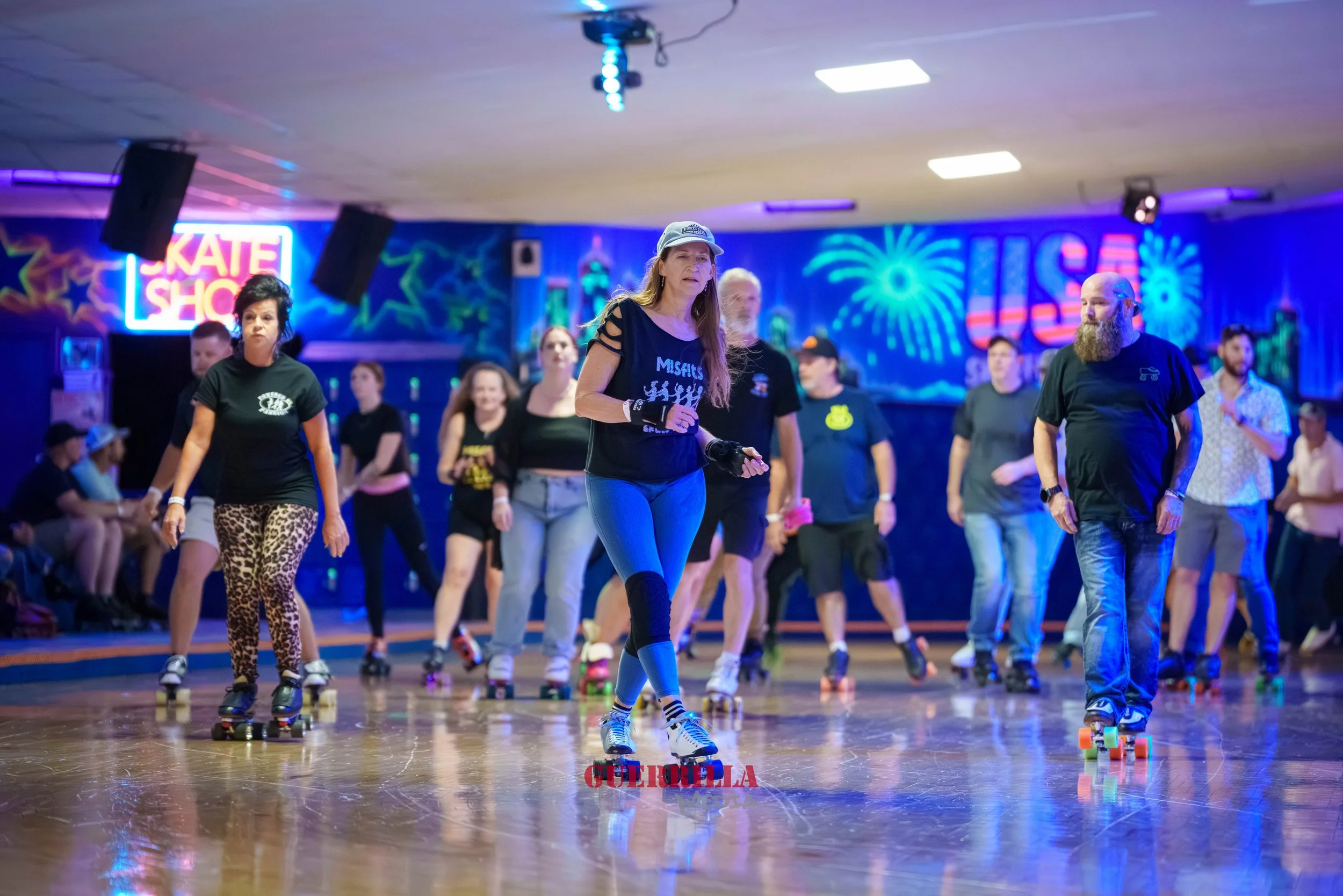 Group of people roller skating in a roller rink with a blue and neon-lit background featuring the words 'Skate Show' and colorful fireworks graphics.