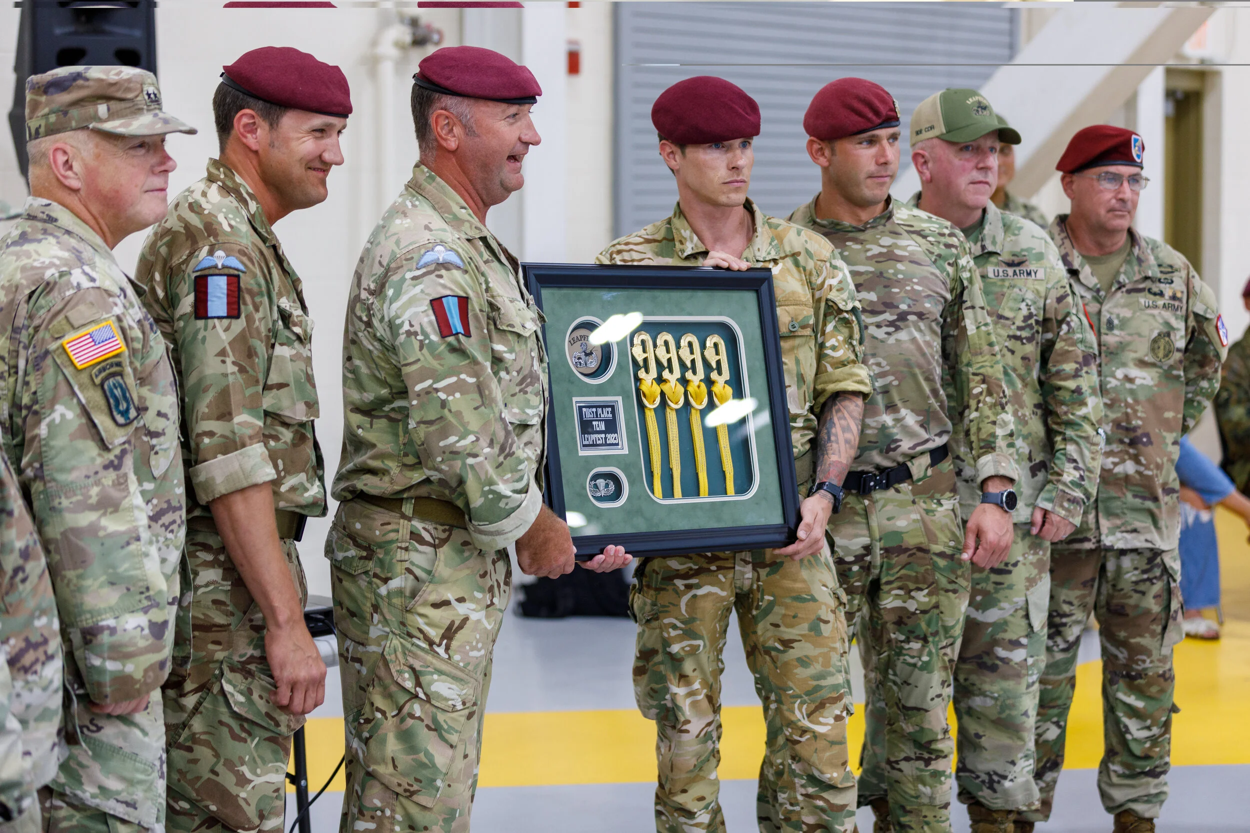 Group of soldiers in camouflage uniforms standing in a line during an award ceremony, with one soldier holding a framed display of medals and ribbons.