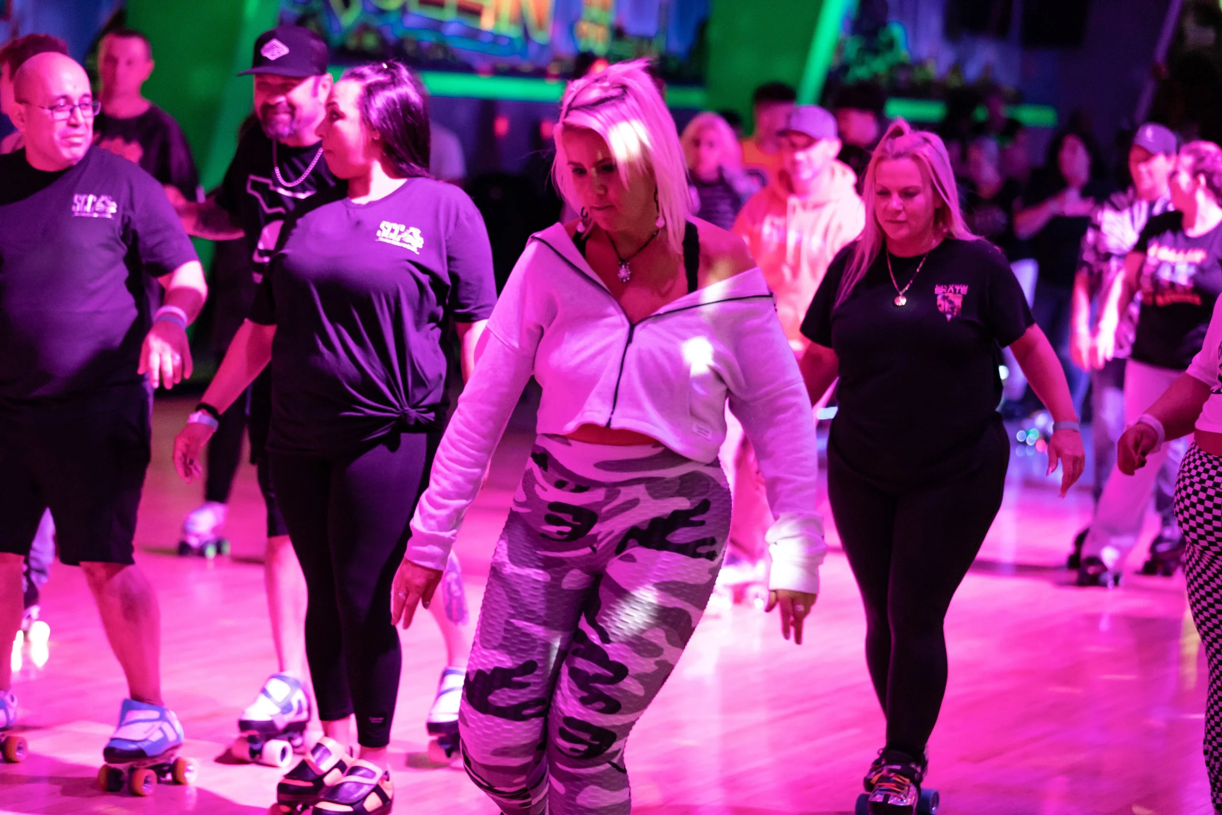 People roller skating at an indoor rink with colorful lighting and neon decorations.
