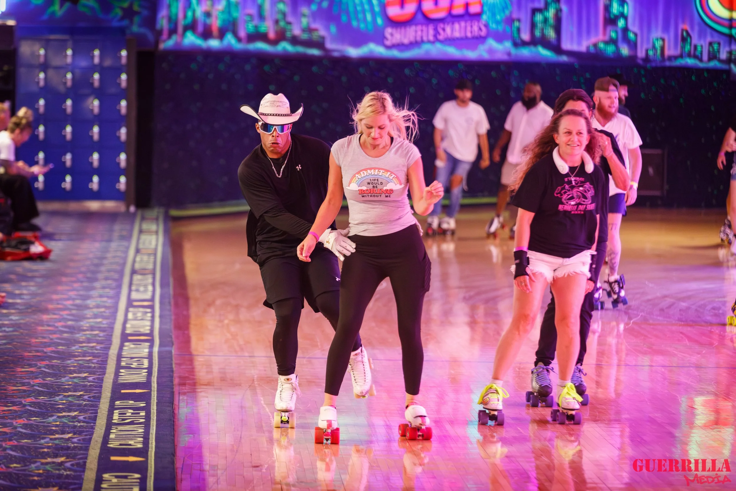 People roller skating on a wooden rink, with a colorful, neon-lit background and lockers visible on the side.