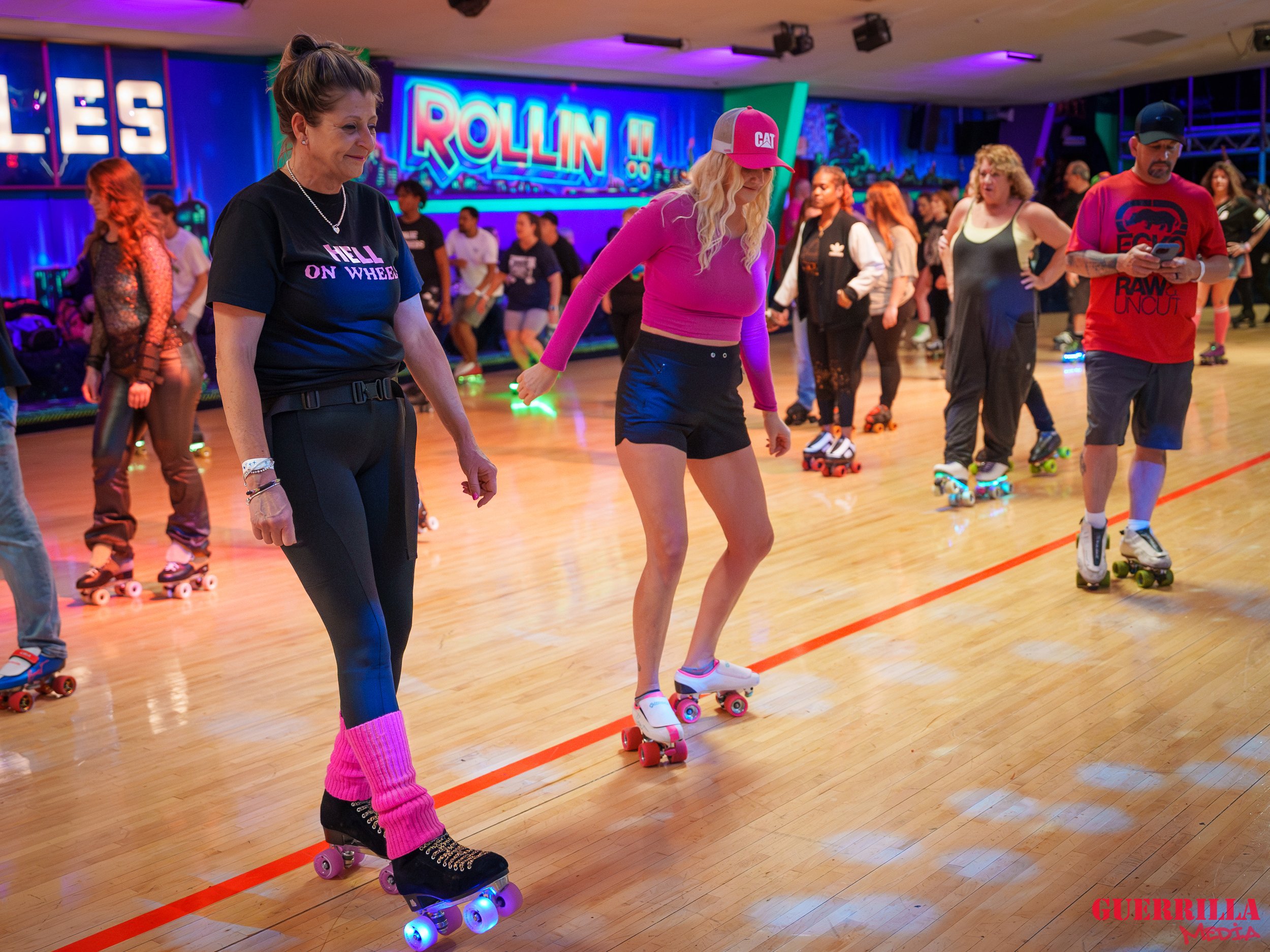 People roller skating in a roller rink with colorful neon lights and a 'ROLLIN' sign in the background.