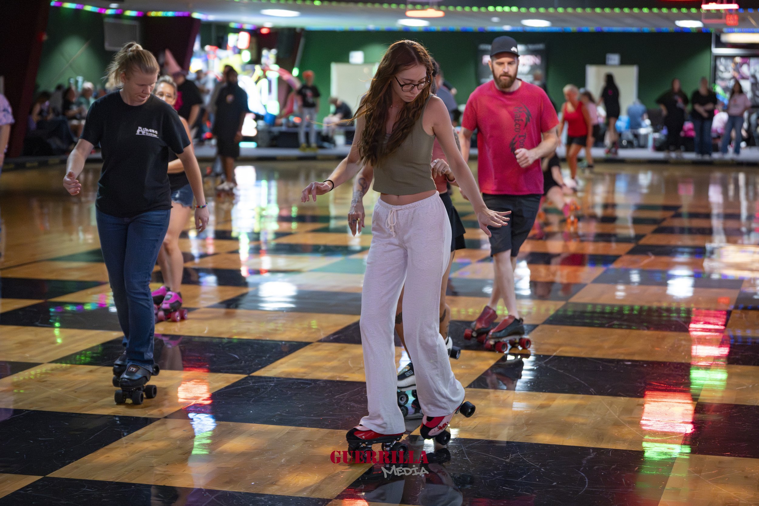 People roller skating on a checkered floor in an indoor skating rink.