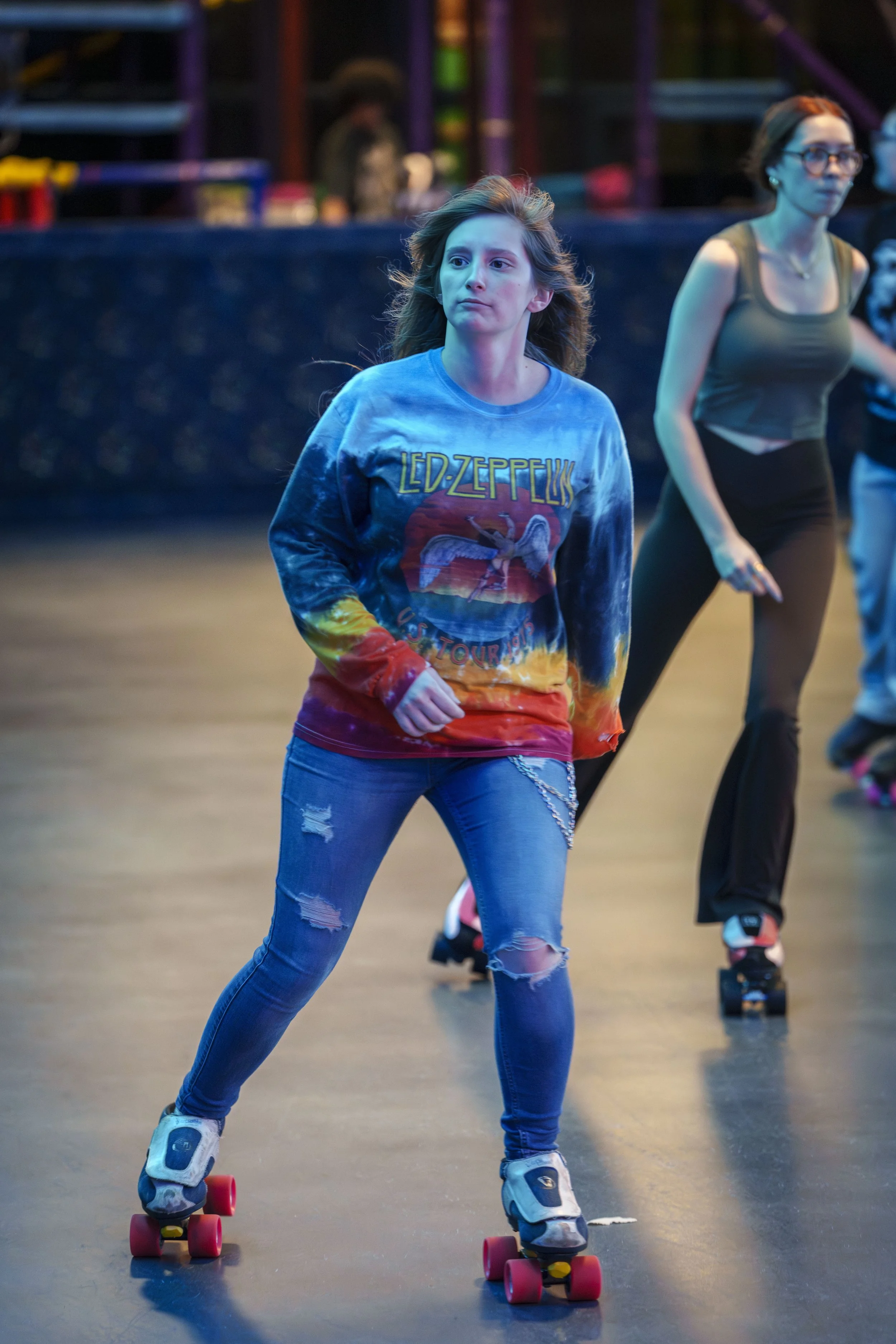 Young girl roller skating indoors, wearing a tie-dye Led Zeppelin t-shirt and ripped jeans.