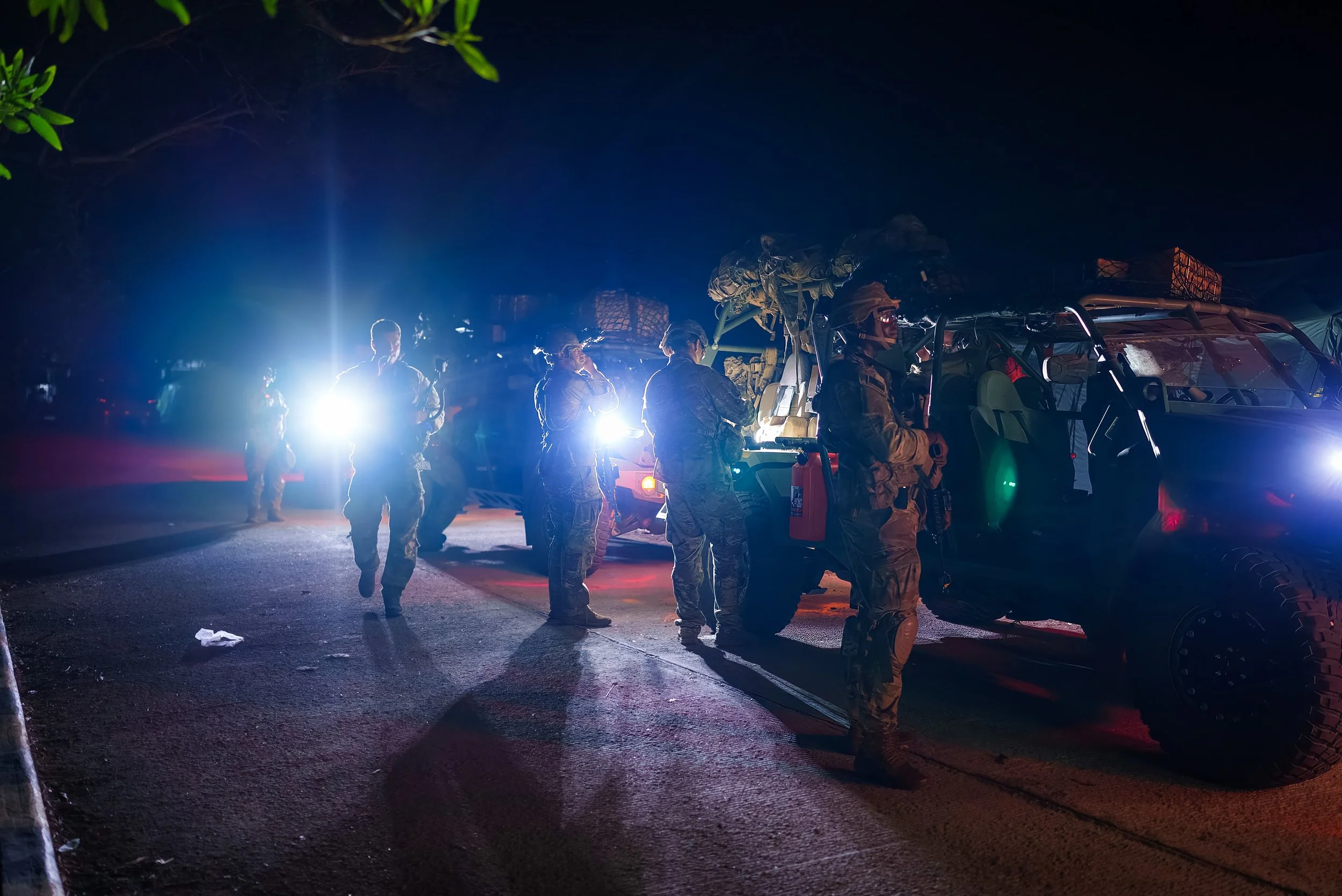 Group of soldiers in military gear standing near an illuminated military vehicle at night.