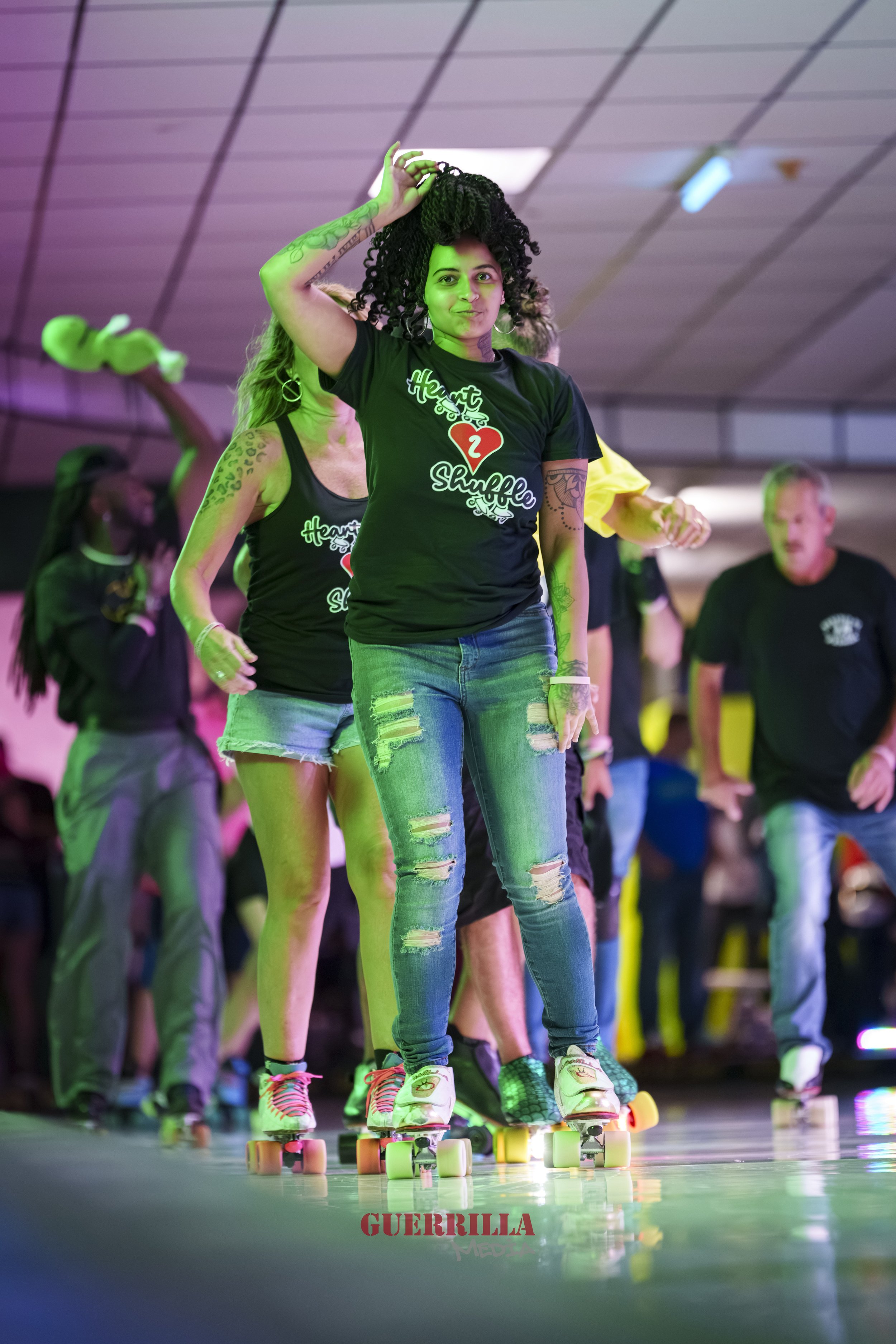 Group of people roller skating indoors, with colorful lighting and casual clothing, including ripped jeans and graphic t-shirts.
