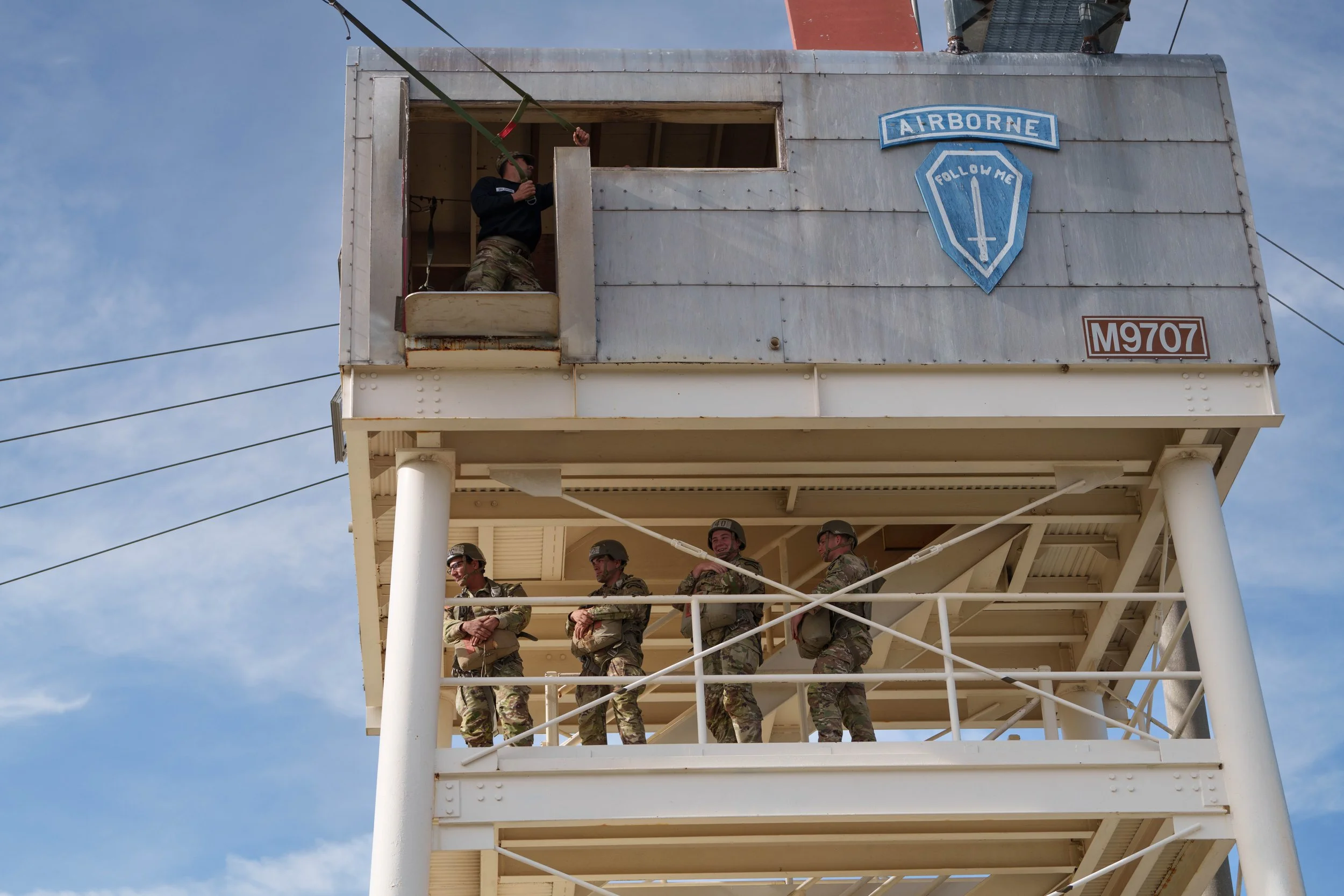 Military personnel practicing on a training tower with an Airborne insignia.