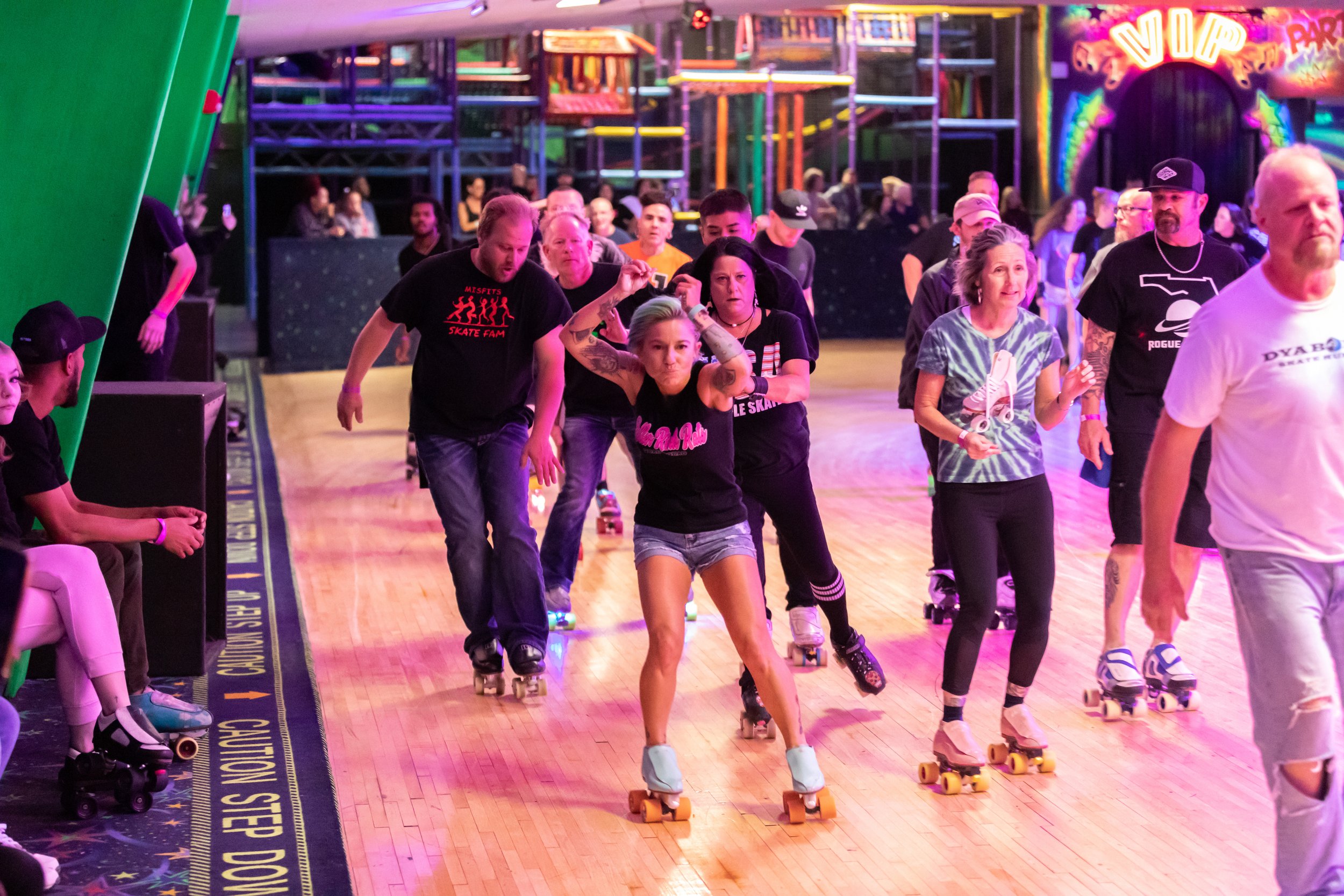 People roller skating indoors at a roller rink with colorful neon lights and a vibrant atmosphere.
