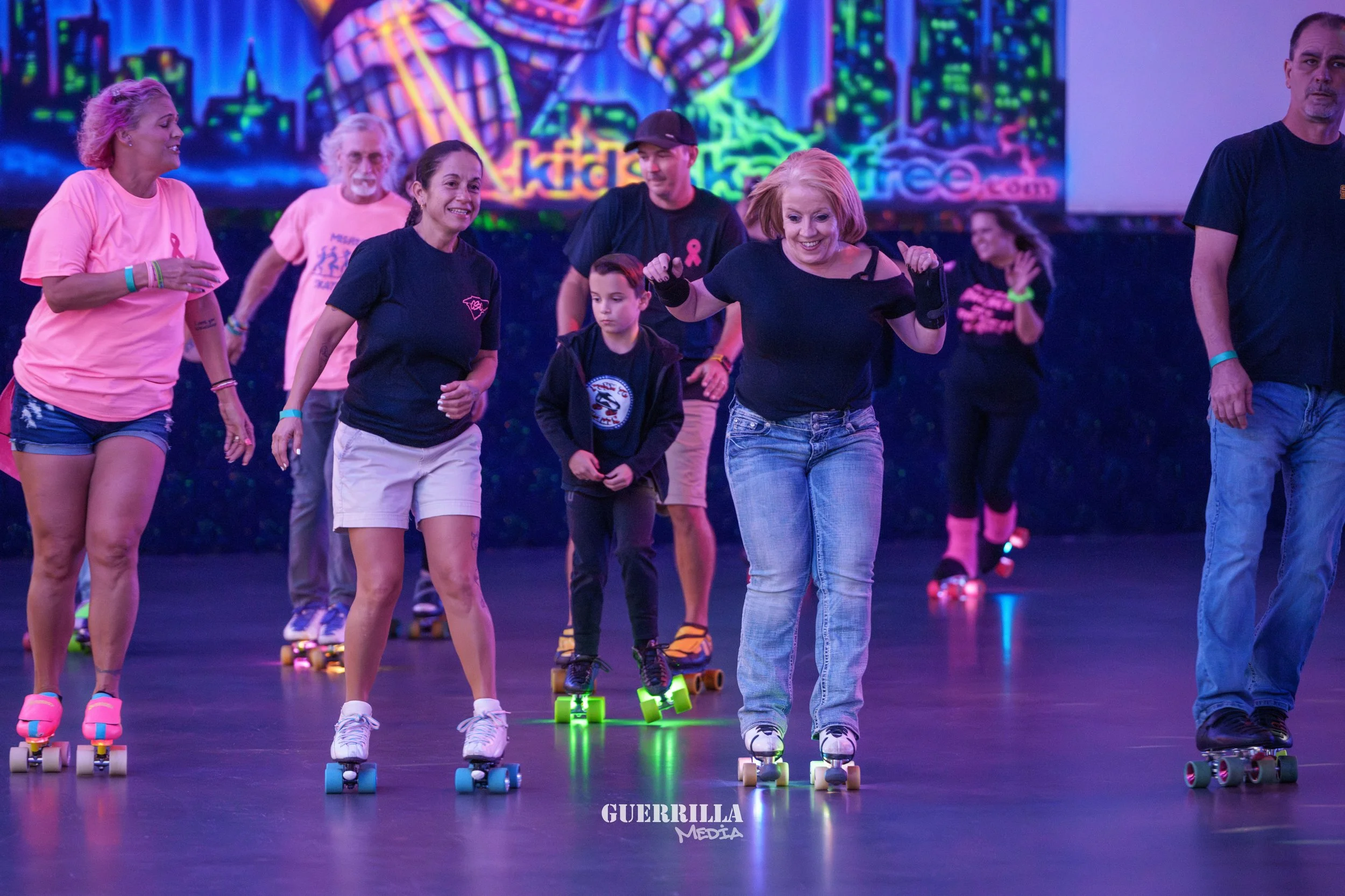 A group of people rollerskating indoors with colorful neon lights and a vibrant background.