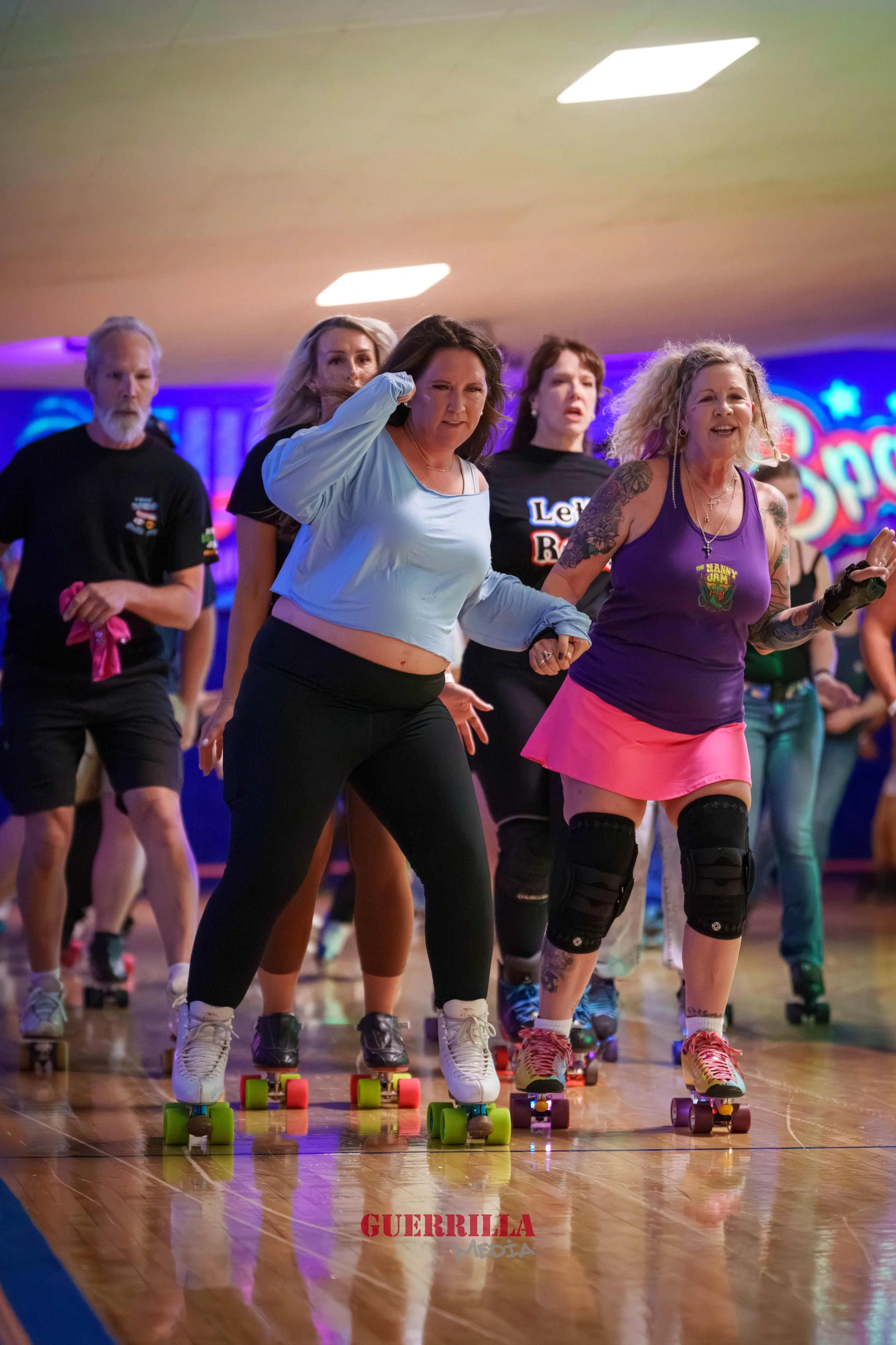 People roller skating indoors at a roller disco event with colorful lighting and a vibrant background.