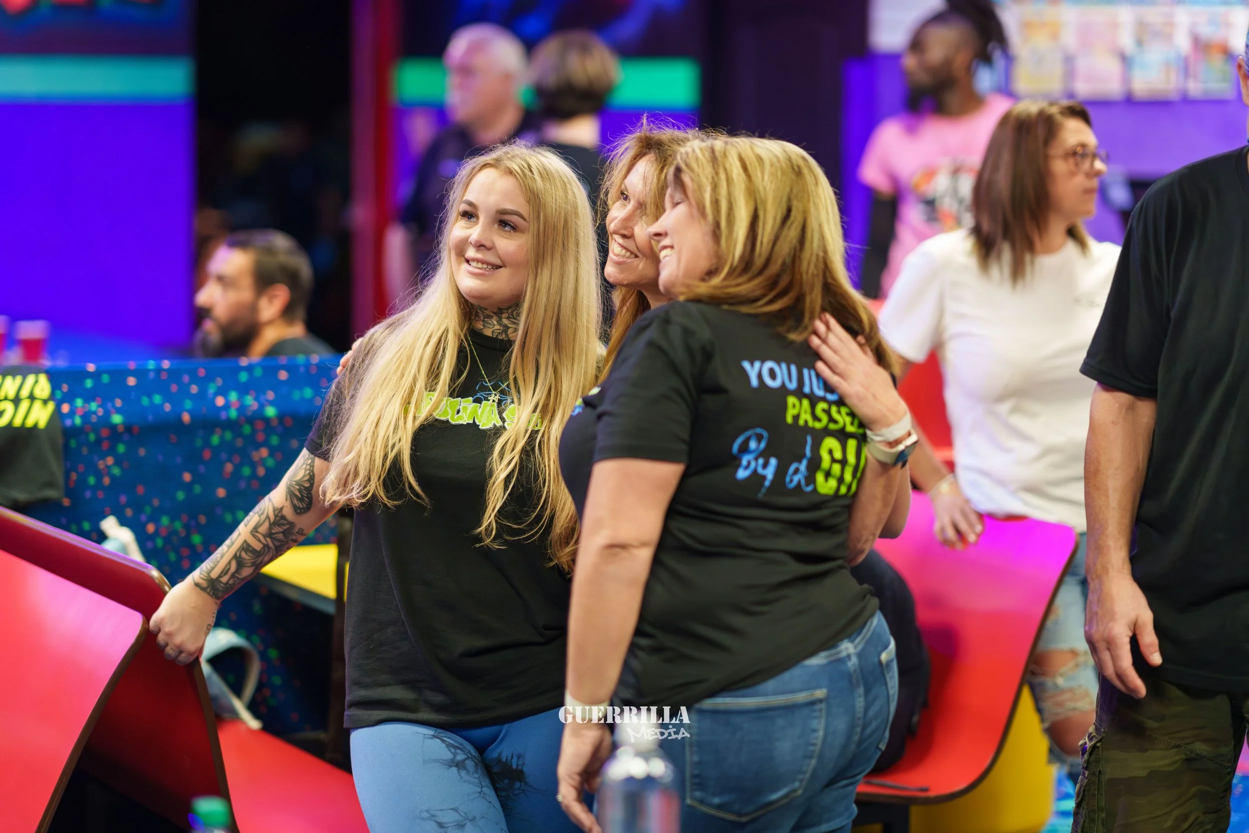 People at a bowling alley, smiling and socializing, with colorful bowling lanes and walls in the background.