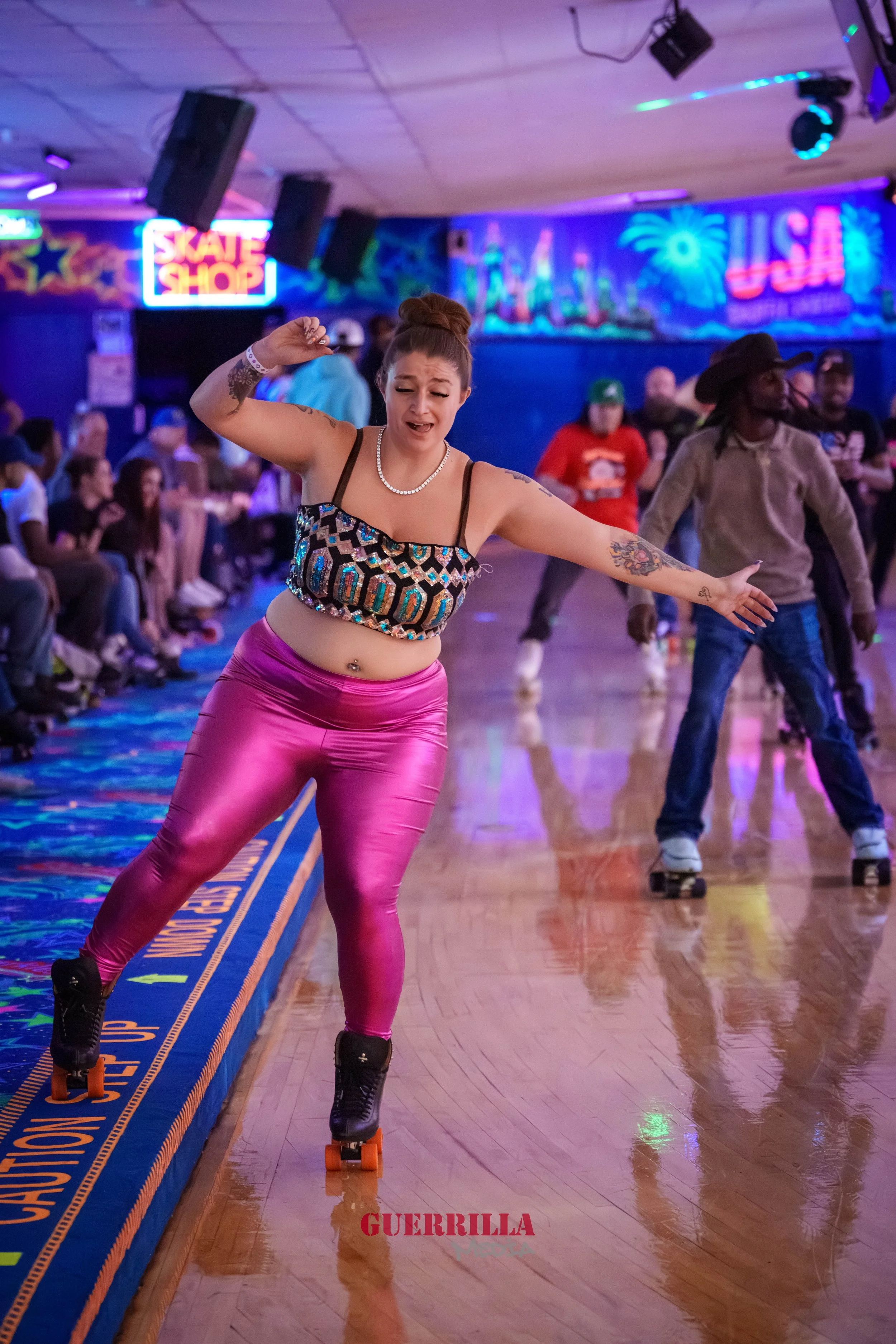 Woman roller skating in an indoor roller rink with colorful neon lights and a mural in the background, surrounded by spectators.