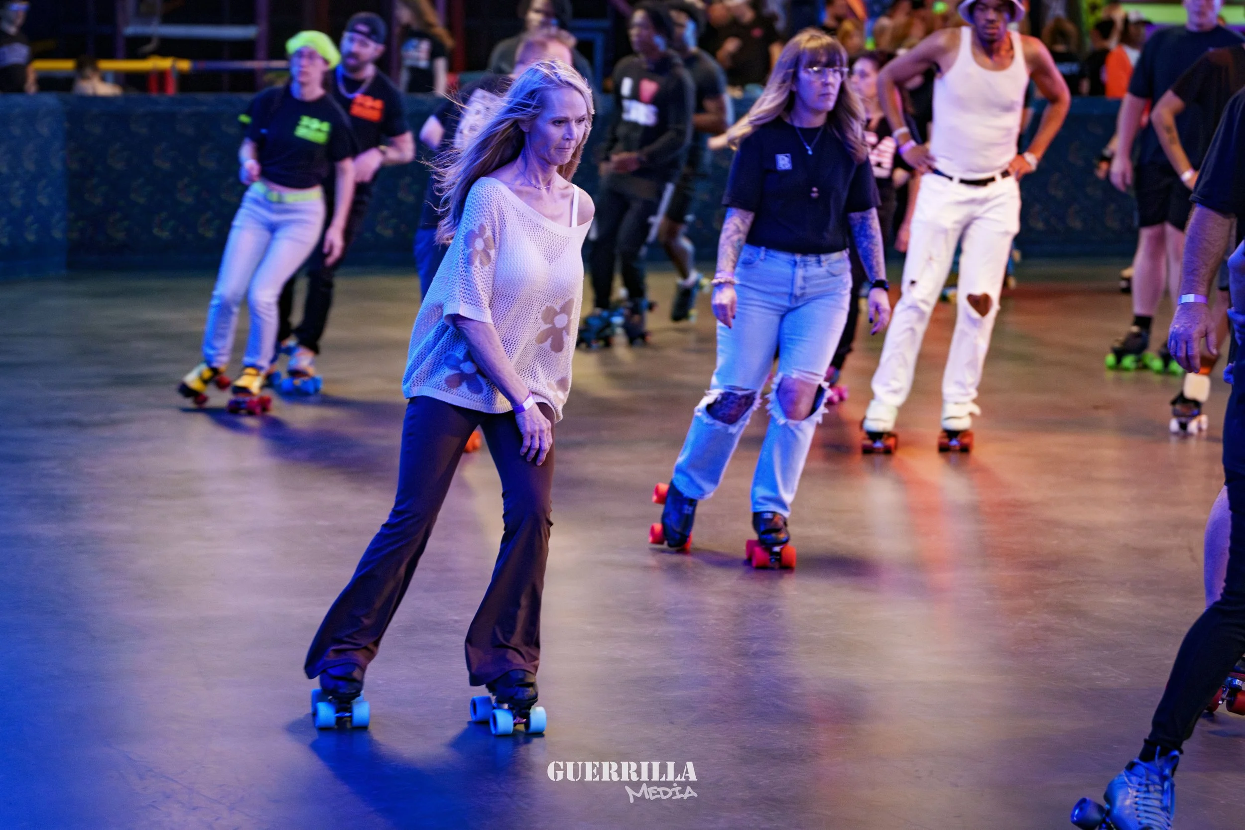 People roller skating together at an indoor rink with colorful lighting.